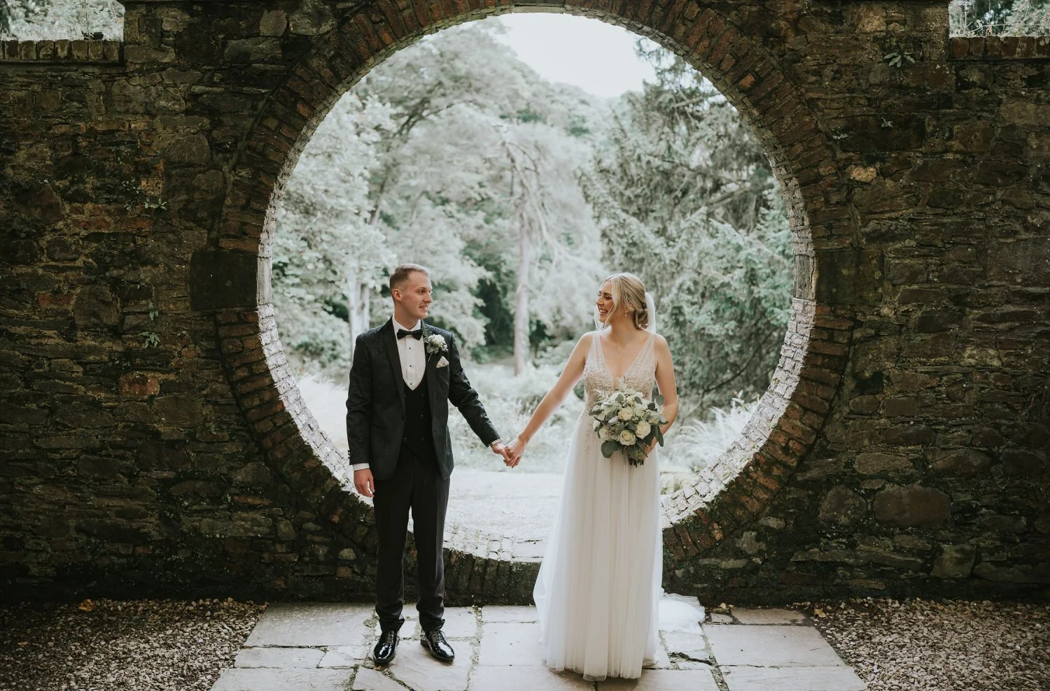 Bride and groom holding hands in front of the circular moon gate in the walled garden at Drenagh Estate, Limavady