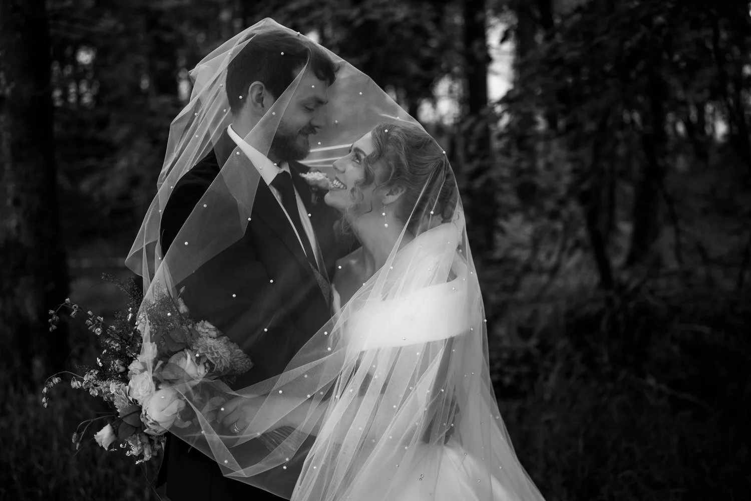 Bride and groom face to face under the bride's veil in the woodland at Glenpark Estate, in black and white
