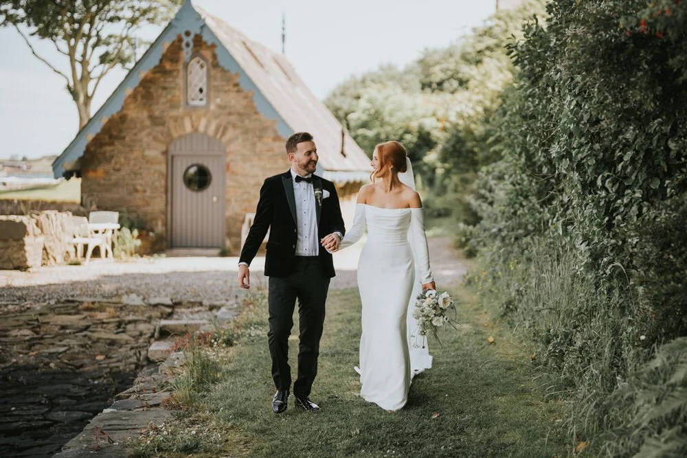 Jenny and Gareth walking hand in hand past the boathouse at Old Court