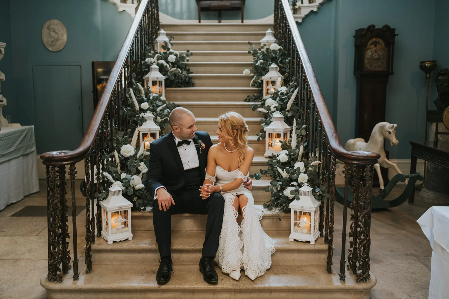 Bride and groom sitting together on the grand staircase surrounded by lanterns in the Georgian house at Drenagh Estate