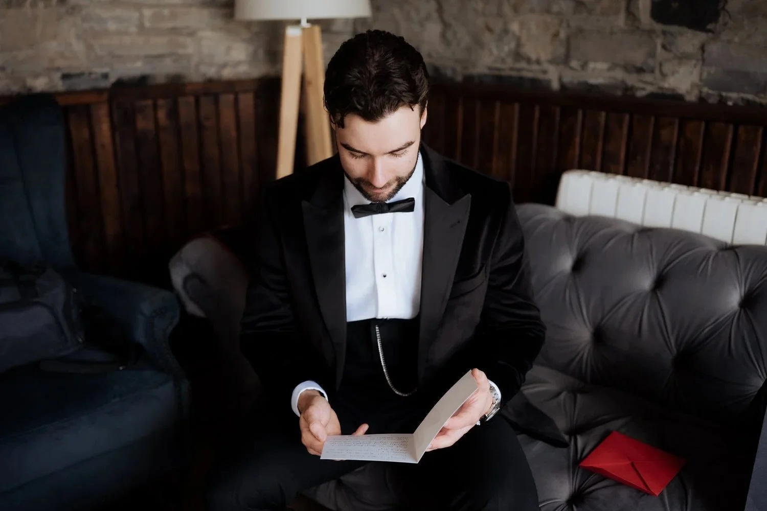 Groom in a black tuxedo reading a letter from his bride on the wedding morning