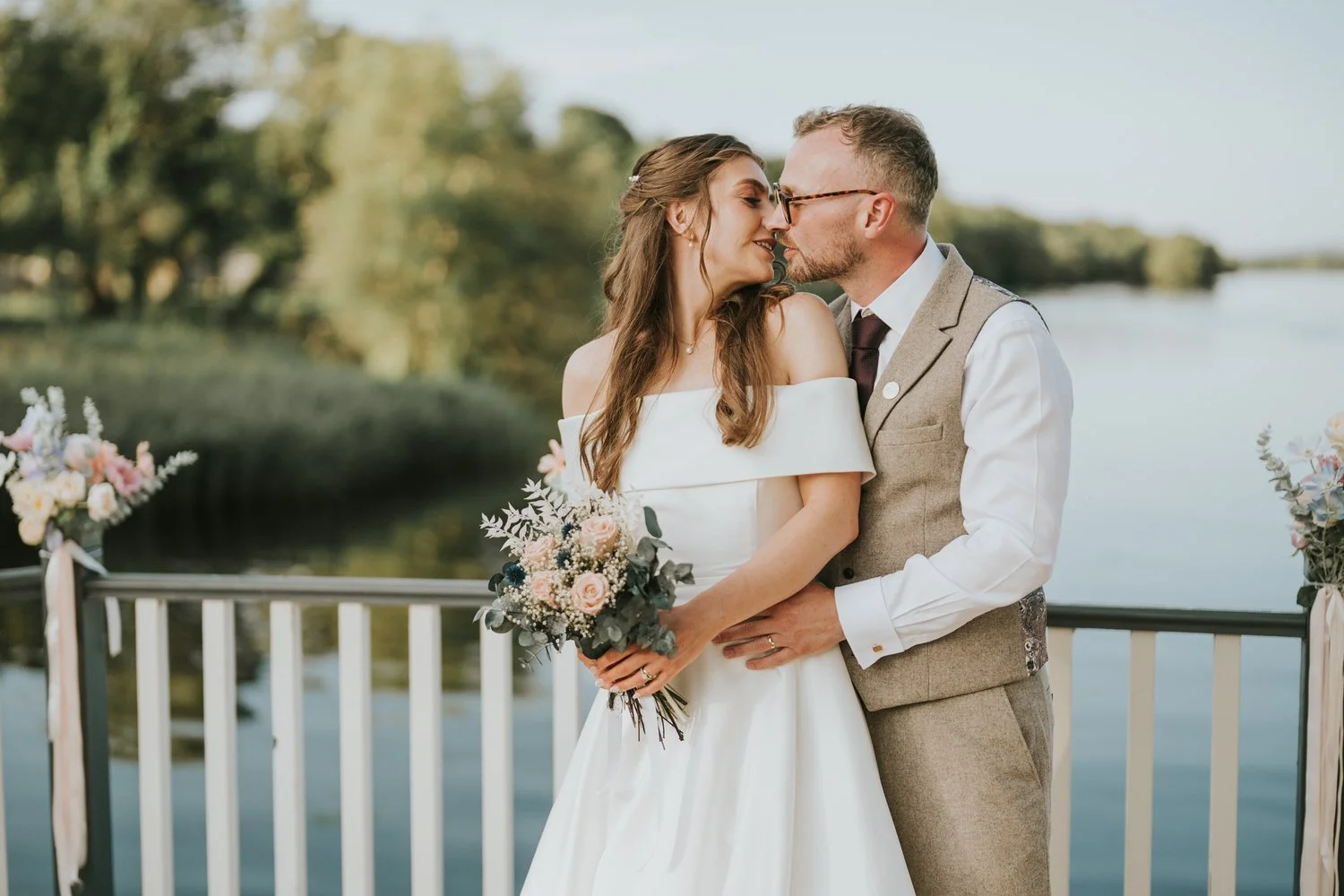 Bride and groom kissing beside a white railing with Lough Erne behind them at Lusty Beg Island