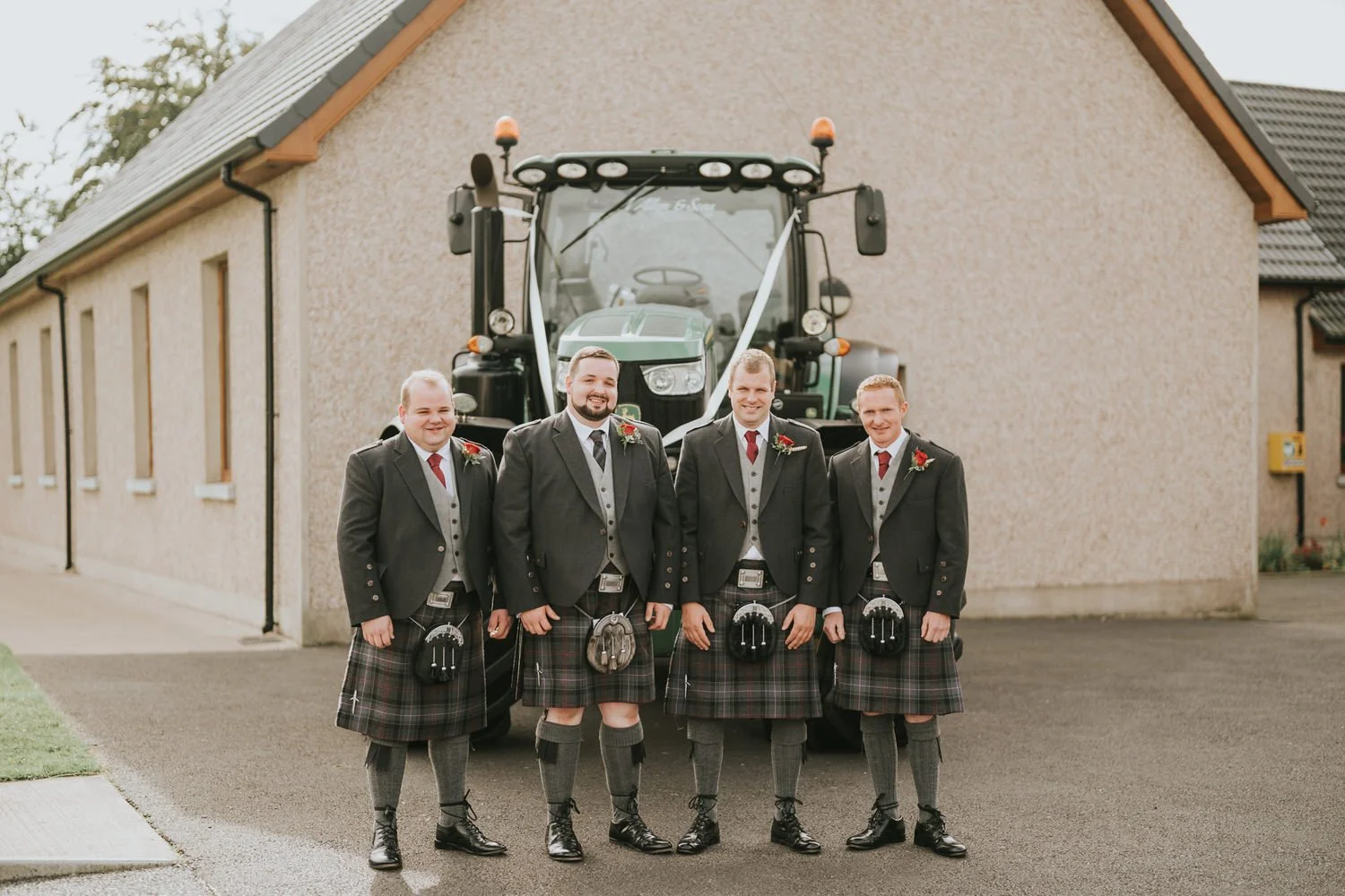 Groomsmen in kilts standing in front of a tractor before a church ceremony