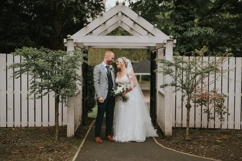 Sophie and Ryan smiling together beneath a white timber archway in the hotel garden