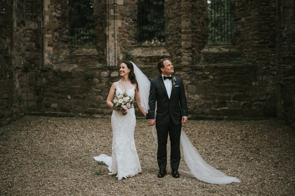 Jennifer and Jeffrey smiling in front of the old stone walls of Greyabbey Abbey