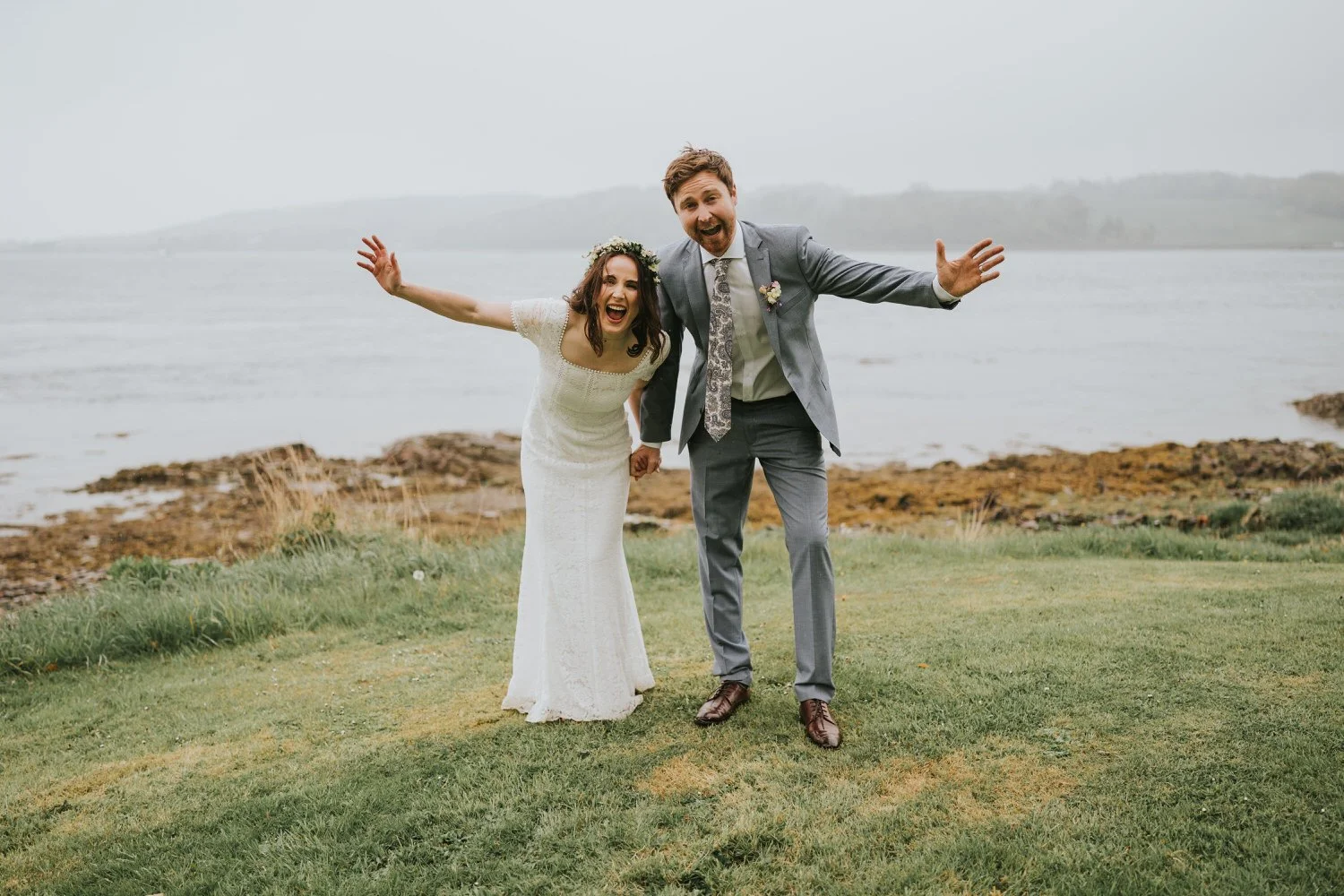 Bride and groom celebrating with their arms raised on the shore of Strangford Lough at Old Court