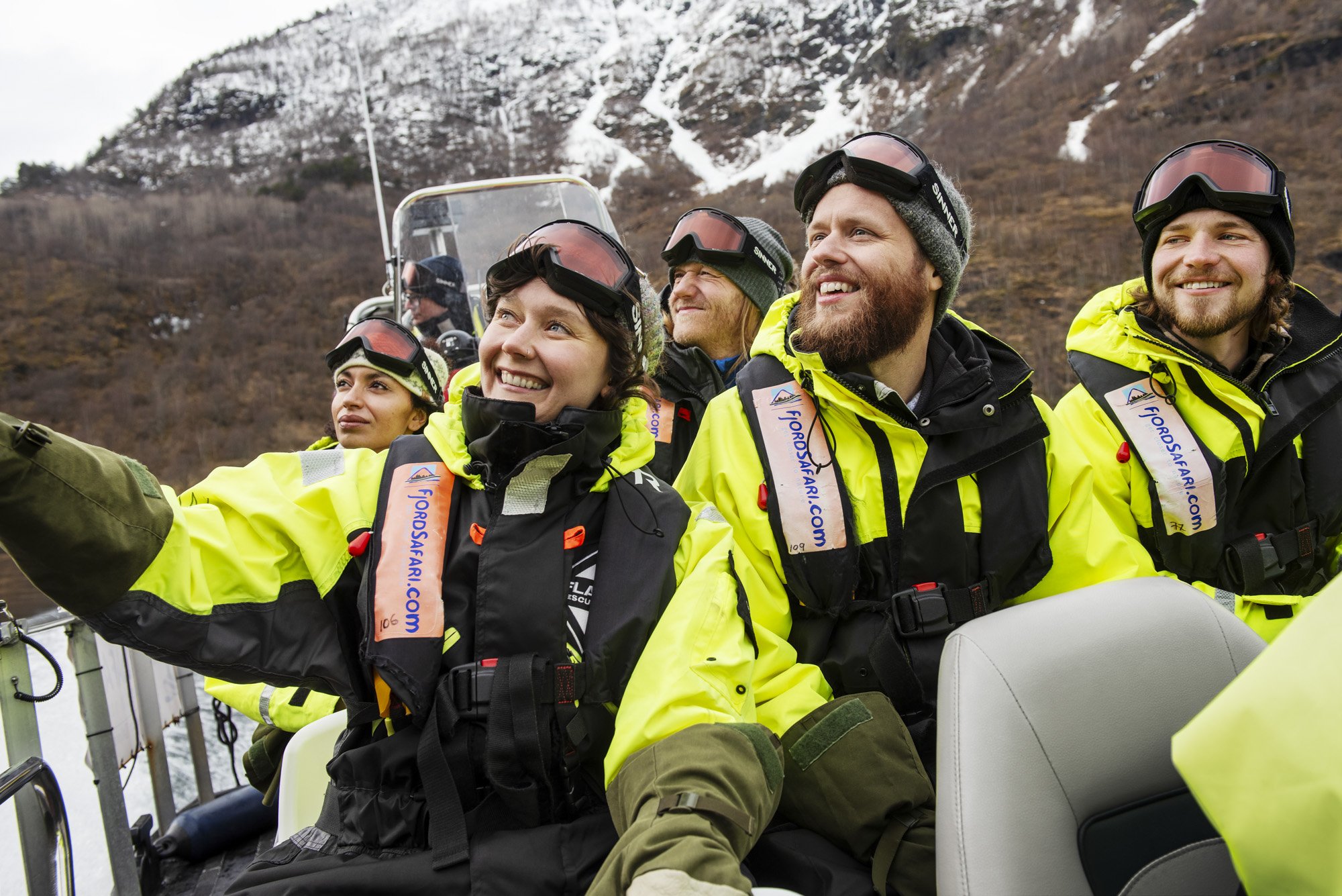 Glade mennesker nyter vinteren Fjordsafari på Aurlandsfjorden. Iført redningsvester og gule flytedrakter.