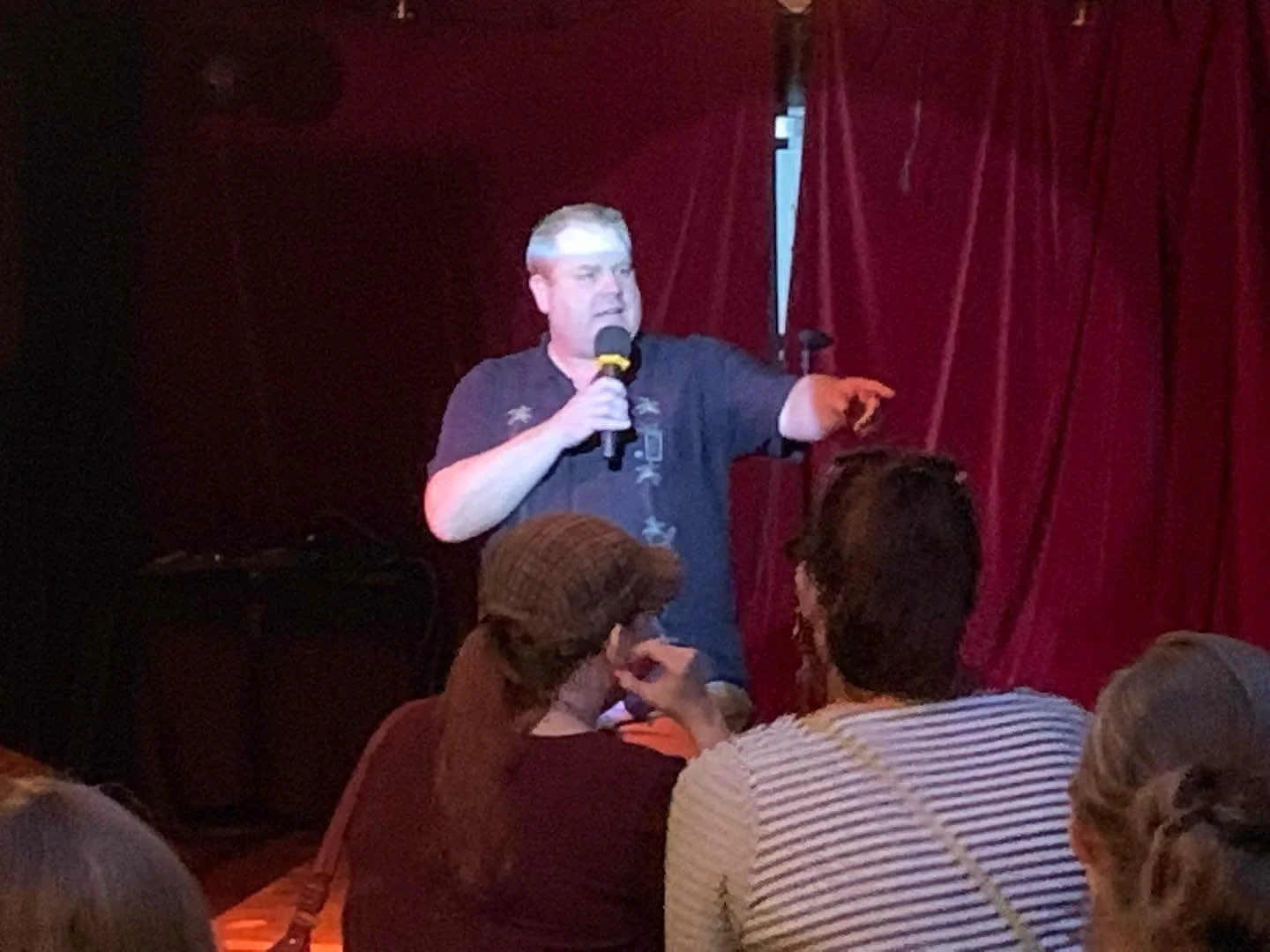 SK Morton holding a microphone, speaking to an audience in front of a red curtain.