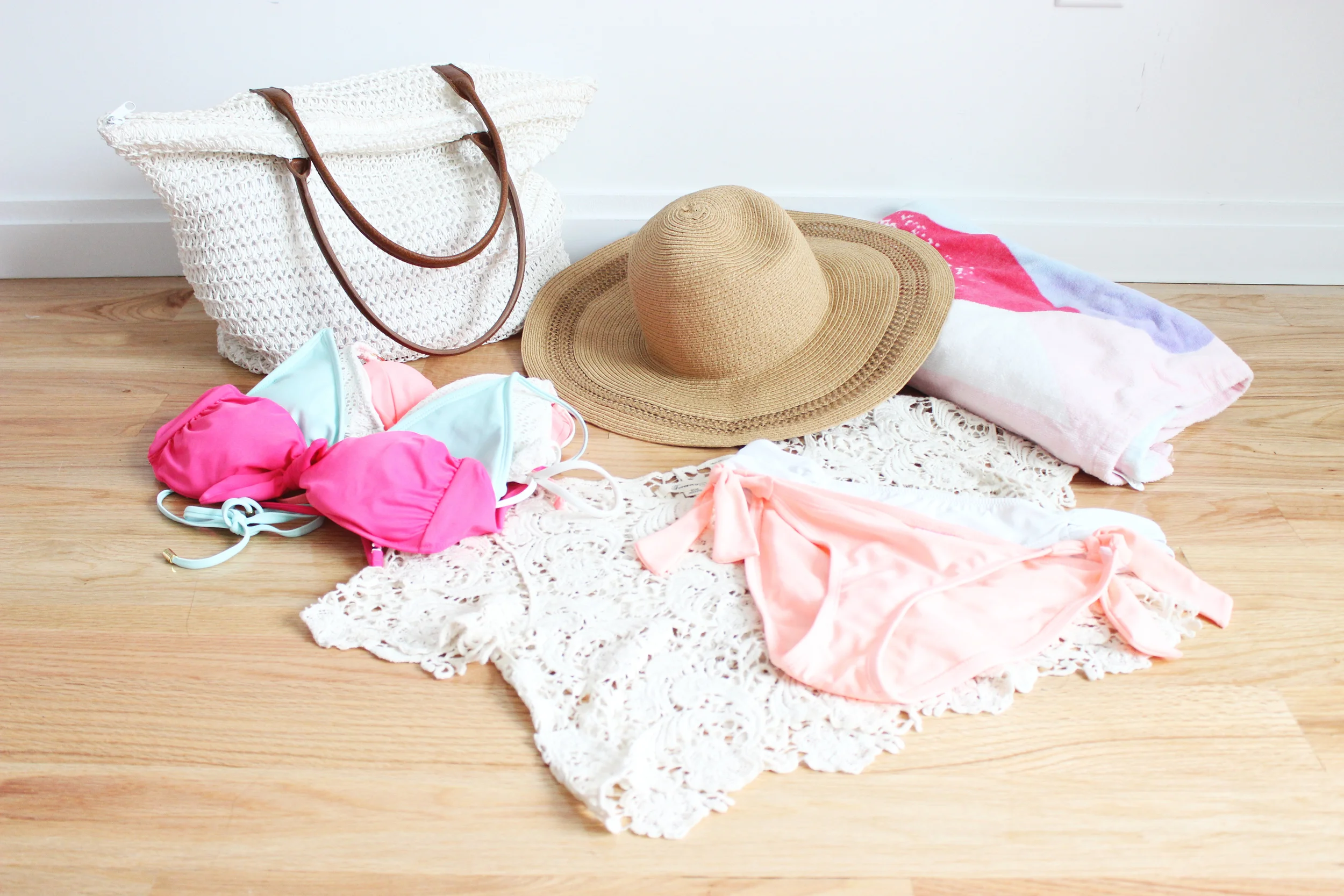 Beach essentials left to right: beach bag, bikinis, sun hat, crop top cover up, bikini bottoms, and beach towel 
