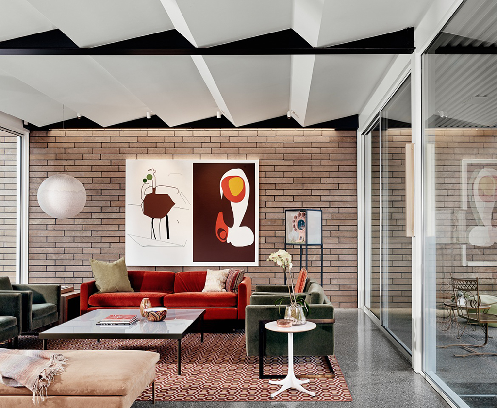Living room with Texas limestone lit by LED wall grazer, exposed steel ceiling beams, acoustic zig zag ceiling, floor to ceiling windows and terrazzo flooring made with marble from Marble Falls, Texas.