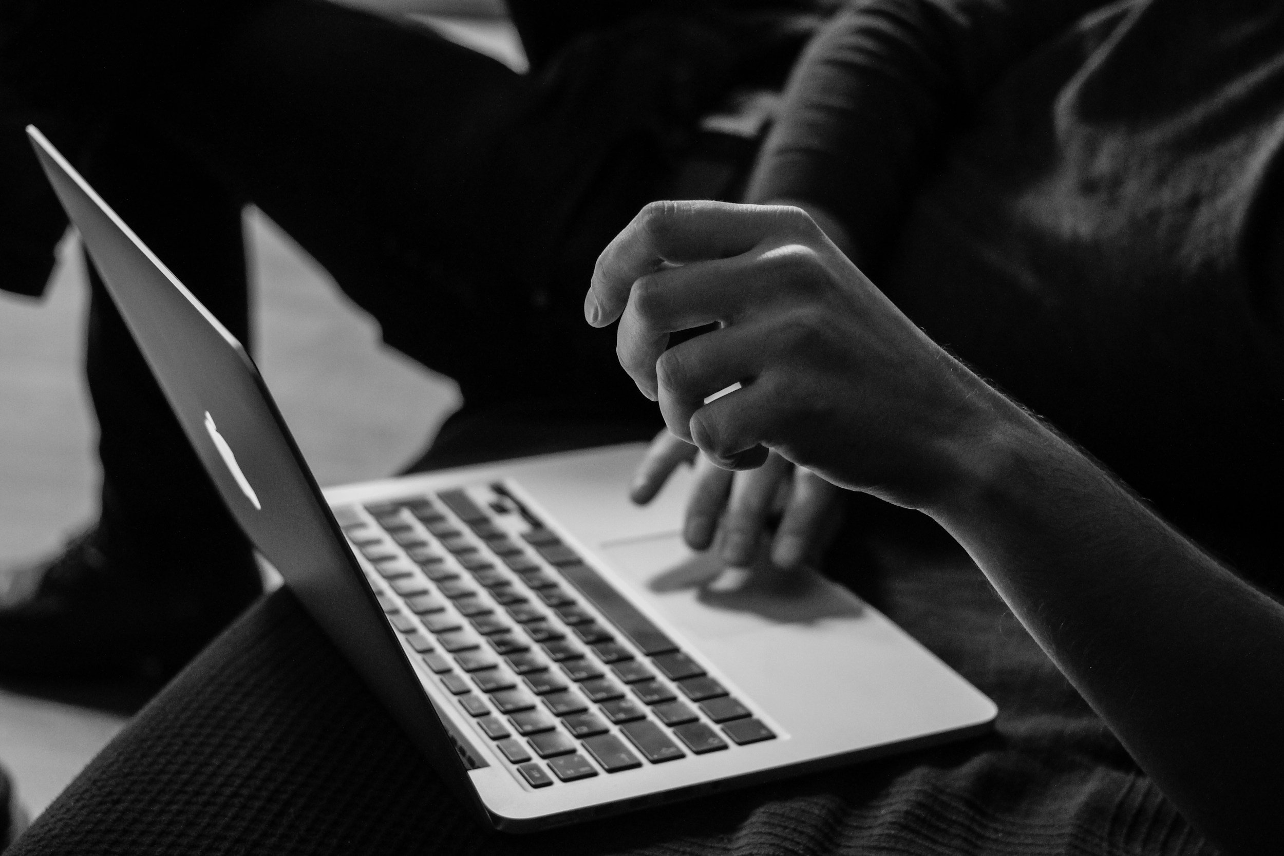Close-up of a person’s hand using a laptop computer in black and white.