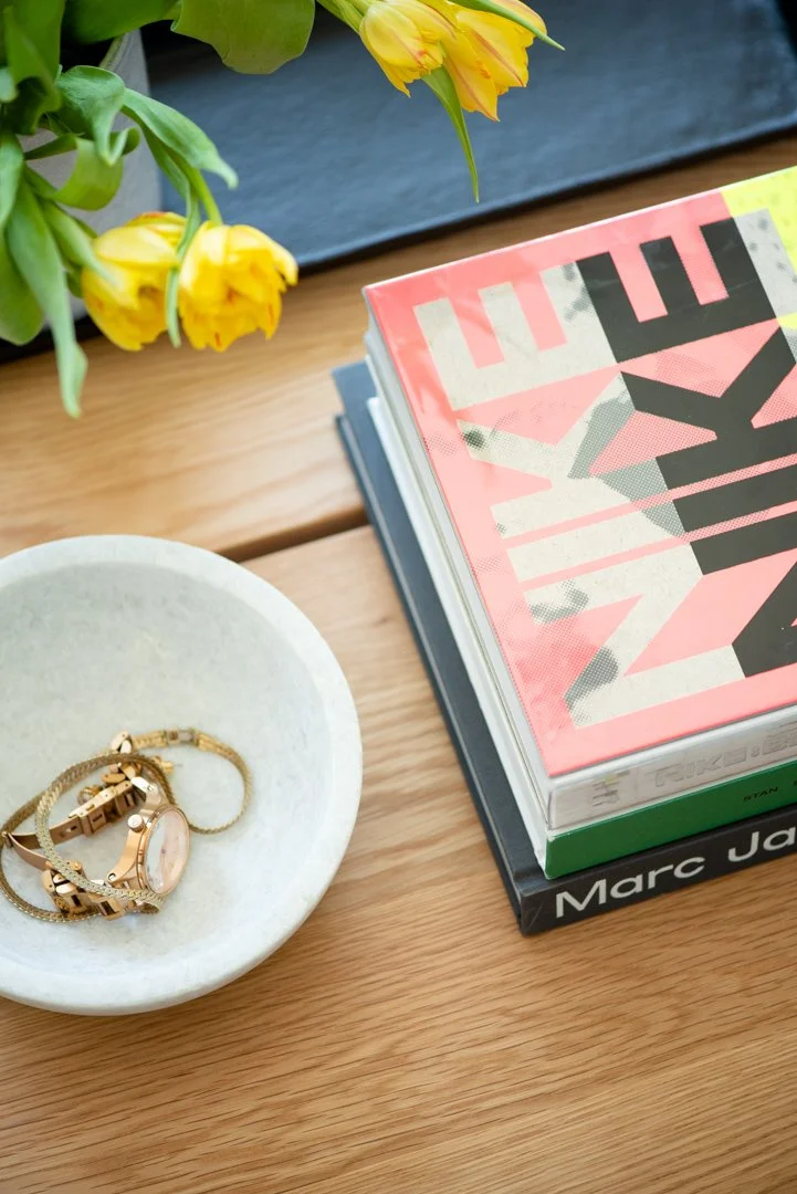 product photography of gold jewelry in a concrete dish sitting on a white oak table with yellow tulips in foreground and bright coffee table books off to the side