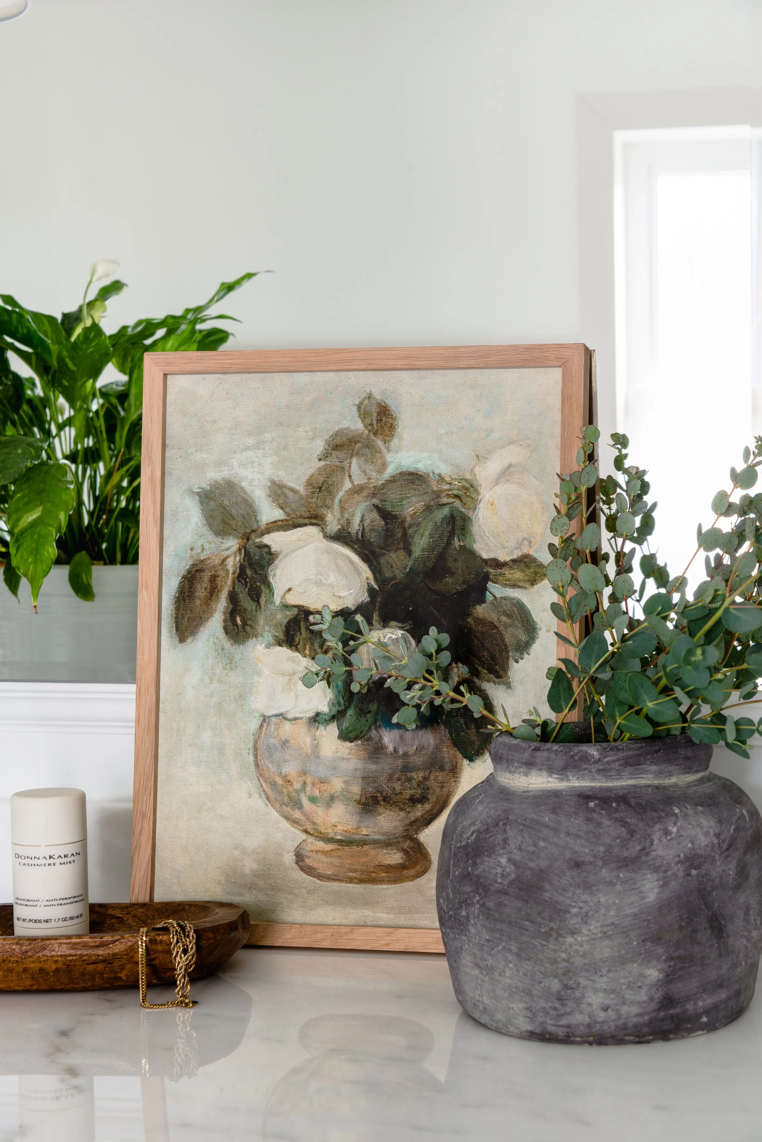 Fine art print styled with foliage on a marble surface with a wooden tray holding anti-perspirant and a gold chain. Product photography