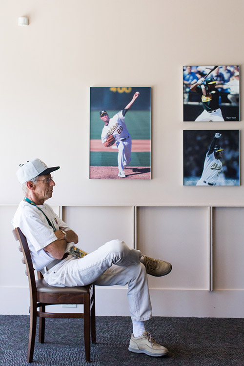 Jim, a season ticket holder, rests and watches the game on a television inside a large enclosed area on the plaza level behind home plate. Pictures of former A's greats hang on the walls. 