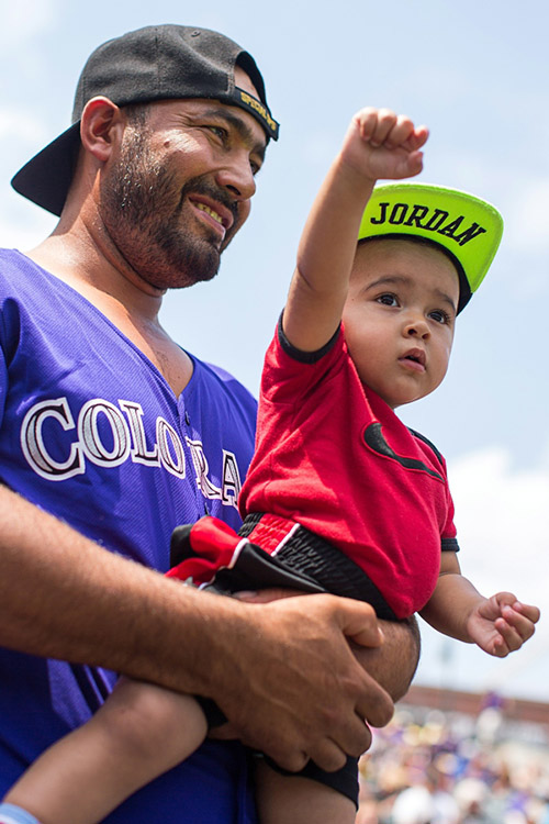 Gael, 1, and Susano watch an on-field kickball game.