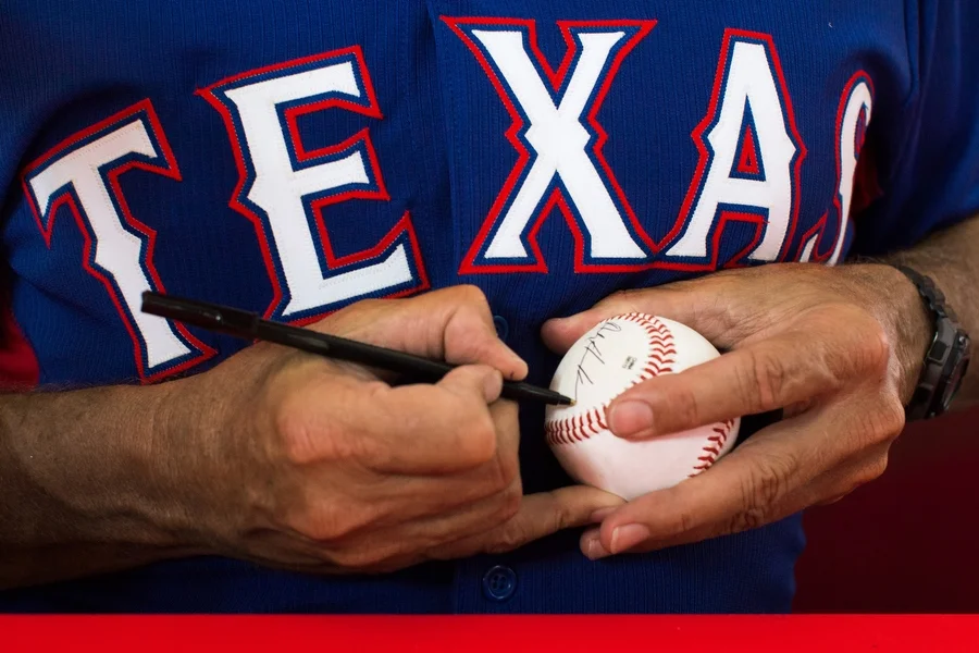 Bullpen coach Andy Hawkins signs a ball. The Rangers host autograph sessions with players and coaches on most Wednesday home games. 