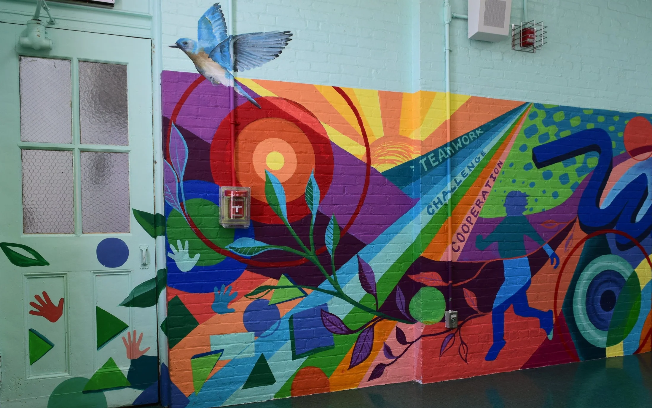 The mural at PS 86 features hand prints, basic shapes, several bulls eyes, a sunrise, and a variety of images drawn from nature.