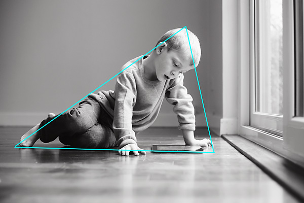 Child laying and looking at a tablet on the ground of a home, illustrating the resemblance of a triangle shape formation within the composition's focus