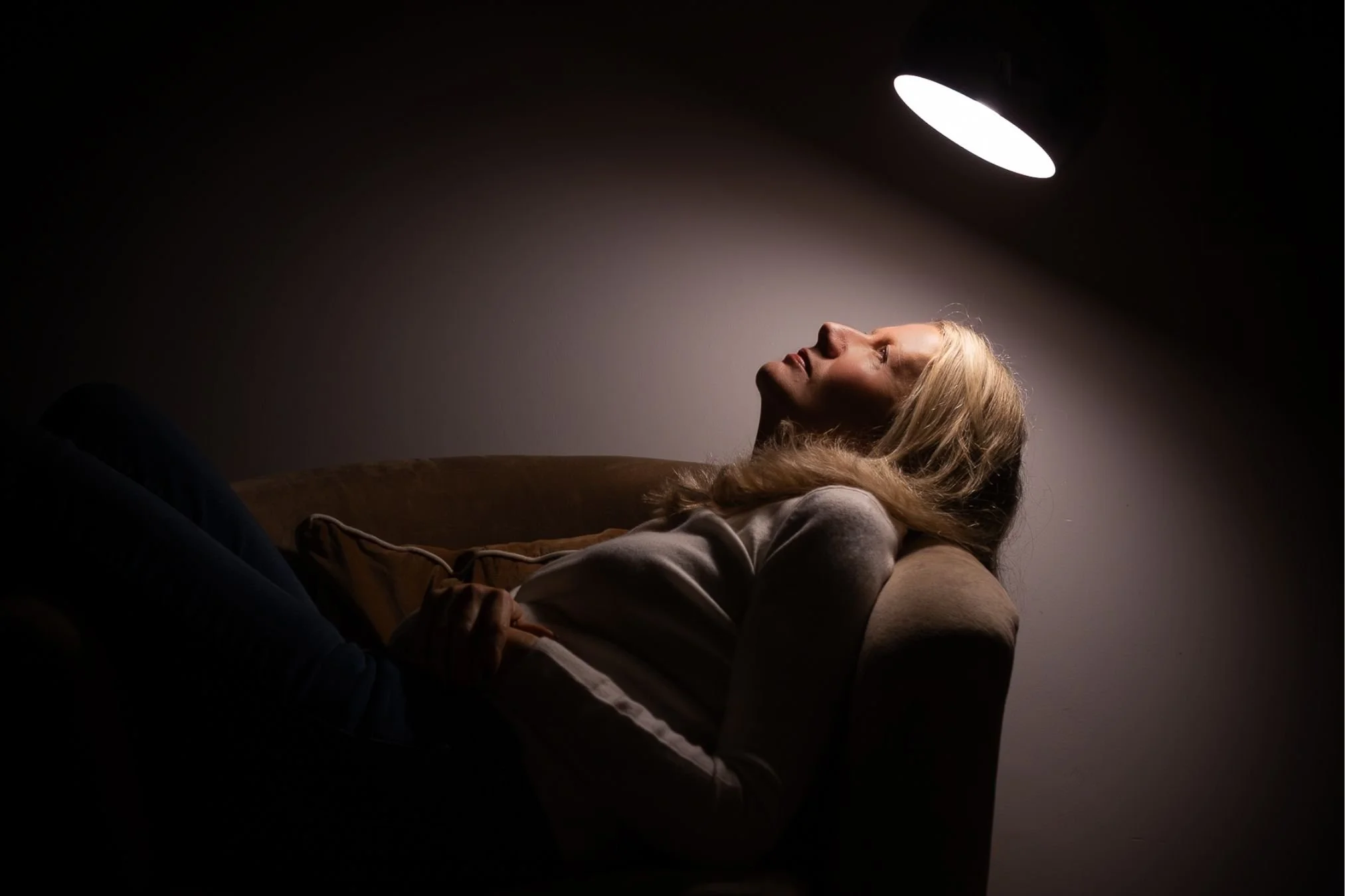 Self-portrait of a woman illuminated by a single lamp in a dark room, demonstrating low light photography using artificial light.