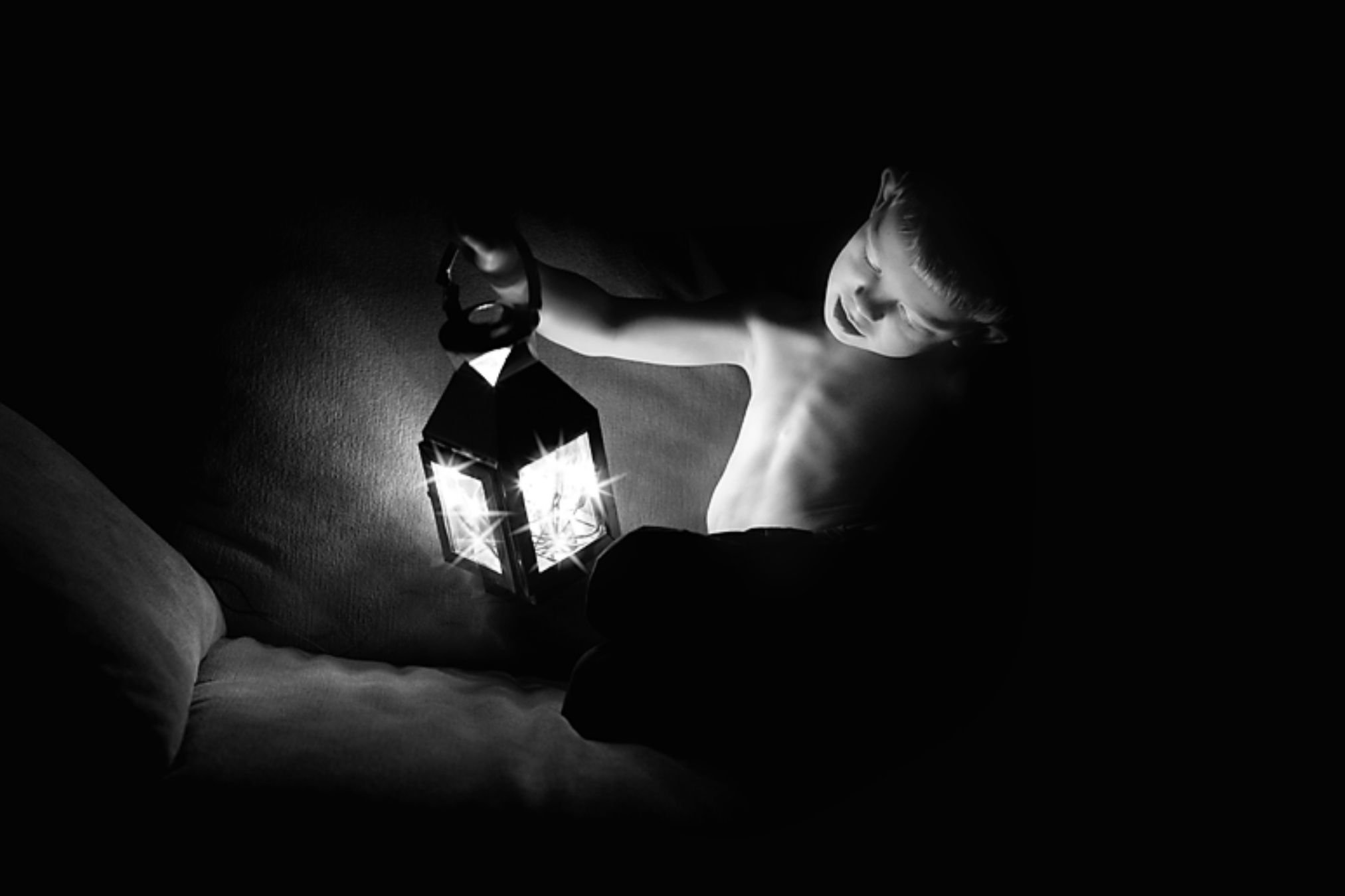 Young boy holding a lantern filled with glowing fairy lights, which illuminate his face against a dark background.