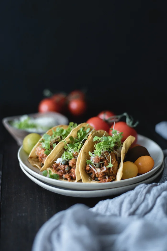 Recipes may come and go, but this one, oh boy, this one is here to stay. This was one of my first recipes on the blog and has been in repeat mode in my kitchen since then. Event though we enjoy very much the typical fresh and raw taco fixings, one day I was craving for something more earthy and creative. Something saucier. I thought of a fish stew infused with lots of Spanish flair. The sauce has chickpeas, capers and sweet piquillo peppers and is seasoned with garlic, saffron and a lot of paprika. Because if there’s a spice that screams Spanish cuisine very loudly it’s paprika, so I wasn’t going to be shy with it. Also, queso Manchego sprinkled on top. For this Cinco de Mayo, which is a Friday so there’s no excuse not to make a fiesta out of it, try something different for your tacos and make this deliciousness instead. I left out a few ingredients from the original recipe and simplified the process a bit. You could have this taco tray in 30 minutes. Promise! All with clean and honest ingredients as always. I used soft corn tortillas but brushed them with a bit of olive oil and toasted them in a non-stick medium skillet. This way they were still soft but with a nice bite and also they didn’t get soggy quickly with the sauce. I served ours with fresh tomato pieces, a dollop of guacamole and sprinkled with queso Manchego. Now all that’s left is mixing an Albariño with some tequila and, believe me, we are going to be all set! Are you ready for the fiesta?! Recipe notes: 1. If using frozen fish meat, submerge the pouches in a medium bowl filled with hot tap water and it will only take minutes to defrost. 2. Depending on the size of the non-stick pan, you can toast a couple of tortillas at a time. Just let them rest on a paper towel while the fish is cooking. 3. Even though I suggested a cooking time for the sauce, you should add the fish at the very last 5 minutes, when you see the sauce is just shy of being very thick. Remember that it will continue thickening while the fish is cooking and it is going to thicken more when it starts to cool down. Spanish fish stew tacos 4 to 6 persons, 12 to 16 stuffed tacos Total time – 30 minutes Cod fillets or other firm white fish - 12 to 16 oz, around 3 to 4 fillets Fine sea salt - 1 Tsp+, divided Fresh ground black pepper – about ½ Tsp, divided Ground or minced garlic – ½ Tsp Extra virgin olive oil - 3 TBS + additional to toast the tortillas Chickpeas – ½ cup Piquillo peppers, chopped in medium pieces - ½ cup Capers - 2 TBSP Fresh chopped Roma or Campari tomatoes – 1 cup Tomato sauce Spanish style or pureed tomatoes (not Italian tomato sauce) - 1 cup Chicken stock (preferably) or water – ½ to 1 cup Saffron threads – ½ Tsp Paprika – 2 TBSP Corn Tortillas Micro cilantro and queso Manchego to serve Season the fish with half of the salt, a pinch of fresh ground pepper and the ground garlic (see notes). In a large skillet heat the olive oil in medium high heat and sauté the chickpeas with ¼ of the salt and a sprinkle of pepper for three minutes approximately, until the chickpeas look caramelized and golden brown on the crust. Add the piquillo peppers and cook two minutes more, until the peppers cook down a bit. Add the capers and tomatoes and sprinkle an extra pinch of salt. Cook for 5 minutes, moving everything frequently, until everything is soft and well integrated. Add the tomato sauce, the chicken stock (or water), the saffron threads, paprika, the rest ¼ of salt and an extra sprinkle of fresh ground pepper. Mix everything well and turn down the heat to medium low. Cook for 15 minutes. In the meantime prepare the tortillas. Heat a non-stick pan in medium high heat. Using a pastry brush cover each tortilla with a bit of olive oil on each side. Place them in the skillet (place as many as you can fit without overlapping them) and cook them for 1 or 2 minutes each side, depending on how quick they are browning. Place them on a paper towel to prevent from becoming soggy with their own steam. When the sauce time's up (see notes), increase the heat again to medium and put the whole fish fillets in the skillet and cook them for about 1 or 2 minutes, then turn them over and cook for a minute or two more. Using a spatula begin to break the fish until lightly shredded, it will continue to break down on its own with the extra heat and extra tossing. Turn down the heat to low and cook until the sauce is thick and the fish is covered by it. Take the fish off the heat and let it rest for a couple of minutes so it absorbs the sauce and cools down a little bit. Serve with the corn tortillas and top with queso Manchego, cilantro leaves or any of your favorite taco fixings.