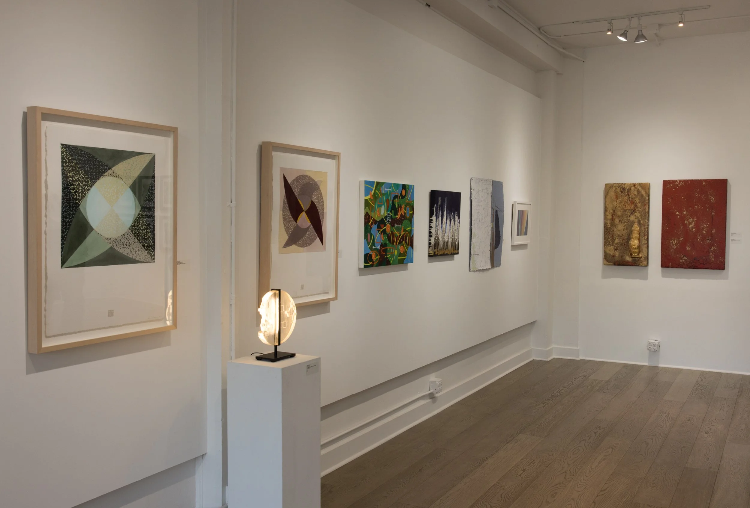 Gallery wall with seven abstract paintings, a small sculpture on a pedestal, and a sculpture in the background.