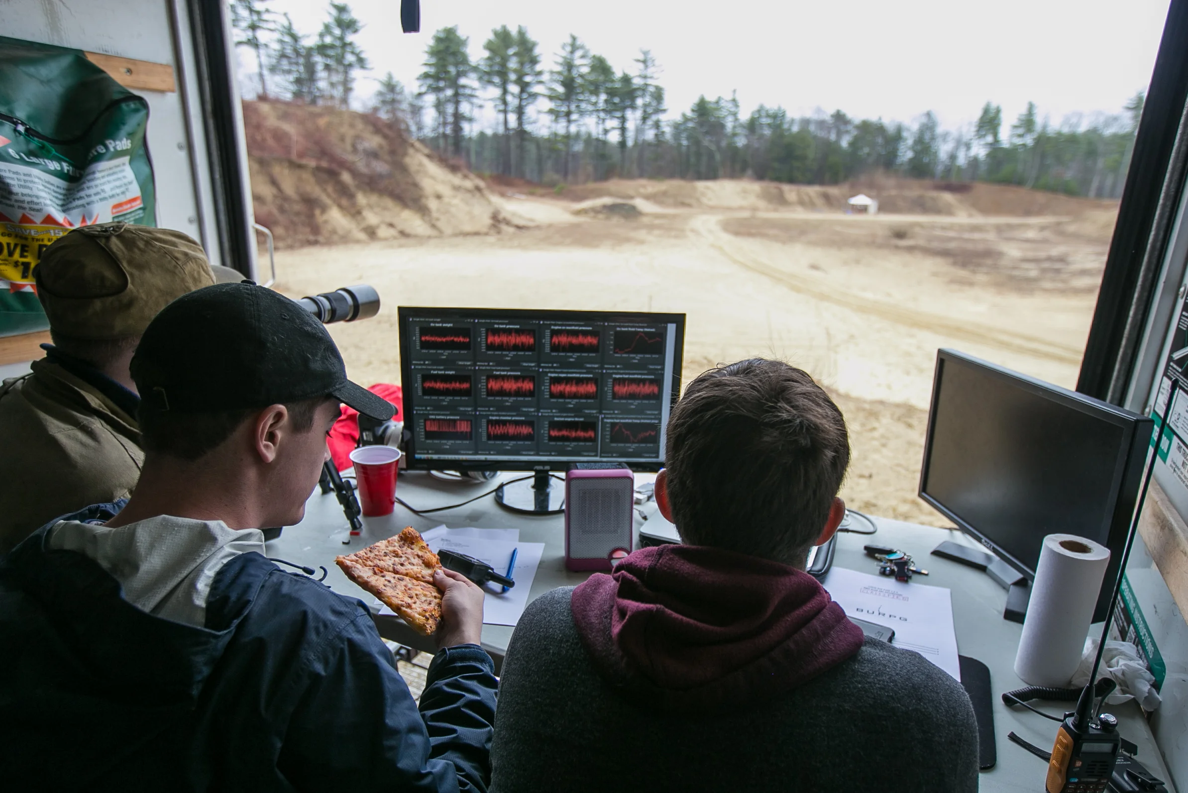 April 2, 2016 – Jeremy Pedro (center), of the Boston University Rocket Propulsion Group, grabs his first slice of pizza as data is recorded after the first successful “hot fire” test of the day. After three aborted attempts, and seven hours of prep, a two-second burn of the newly developed Lotus engine was achieved. Pedro and a team of around 15 engineers had been working since 11pm the previous night to complete the test. “We didn’t quit until 6am this morning,” Pedro said. “40 minutes of sleep, a quick coffee, and we were out here by 8:00am.” Sleepless nights like these are common for the Boston University team as they race the University of Southern California to be the first student designed and constructed rocket to reach space – or about 62 miles above the earth’s surface. © Mike Schwarz