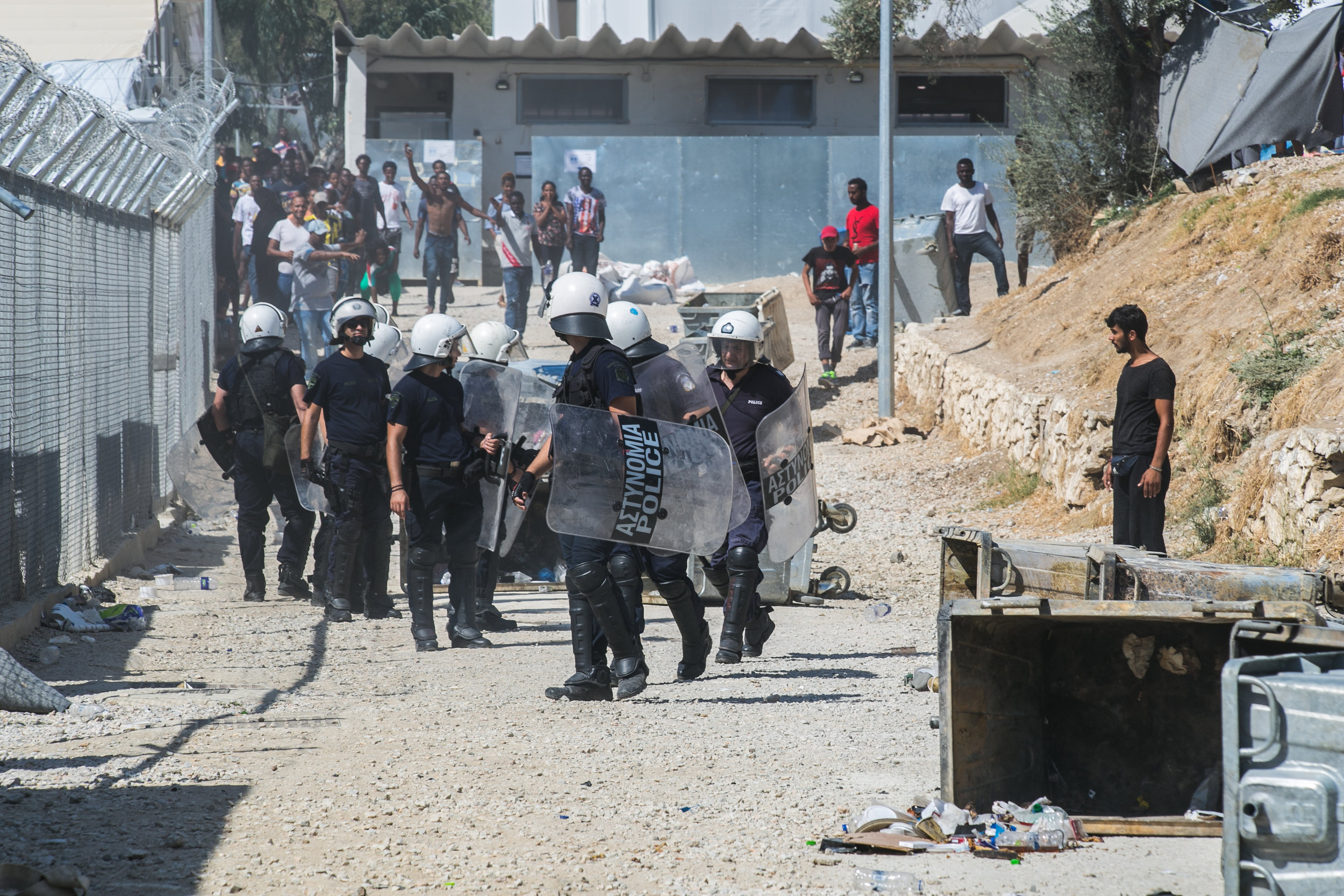   mikeschwarzthekid Riot police react as a crowd of Turkish and Syrian refugees begin to throw rocks outside the entrance to a camp in Moria, Lesvos. The riot began earlier this morning with refugees flipping dumpsters, lighting trash on fire, and ta