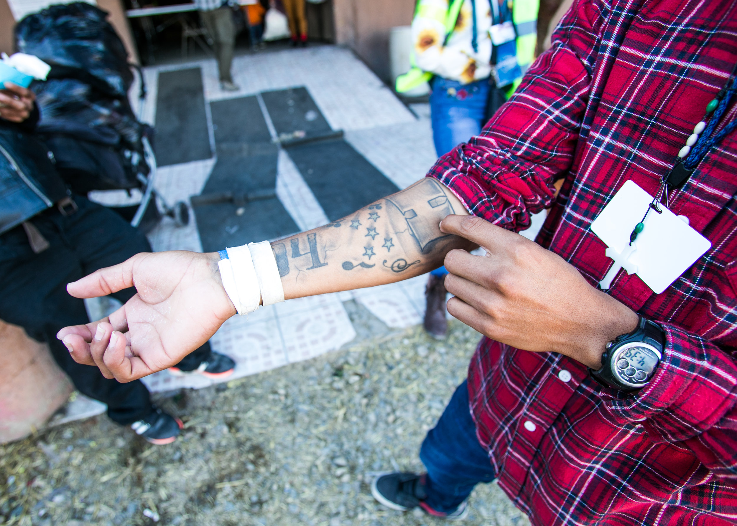  Kevin Hernandez, 19, of Honduras, rolls up his sleeve to show off the tattoos he got several years prior. The numbers hidden by the camp passes on his wrist is the area code of his family home in Honduras. The "H" directly above it (on his forearm) 