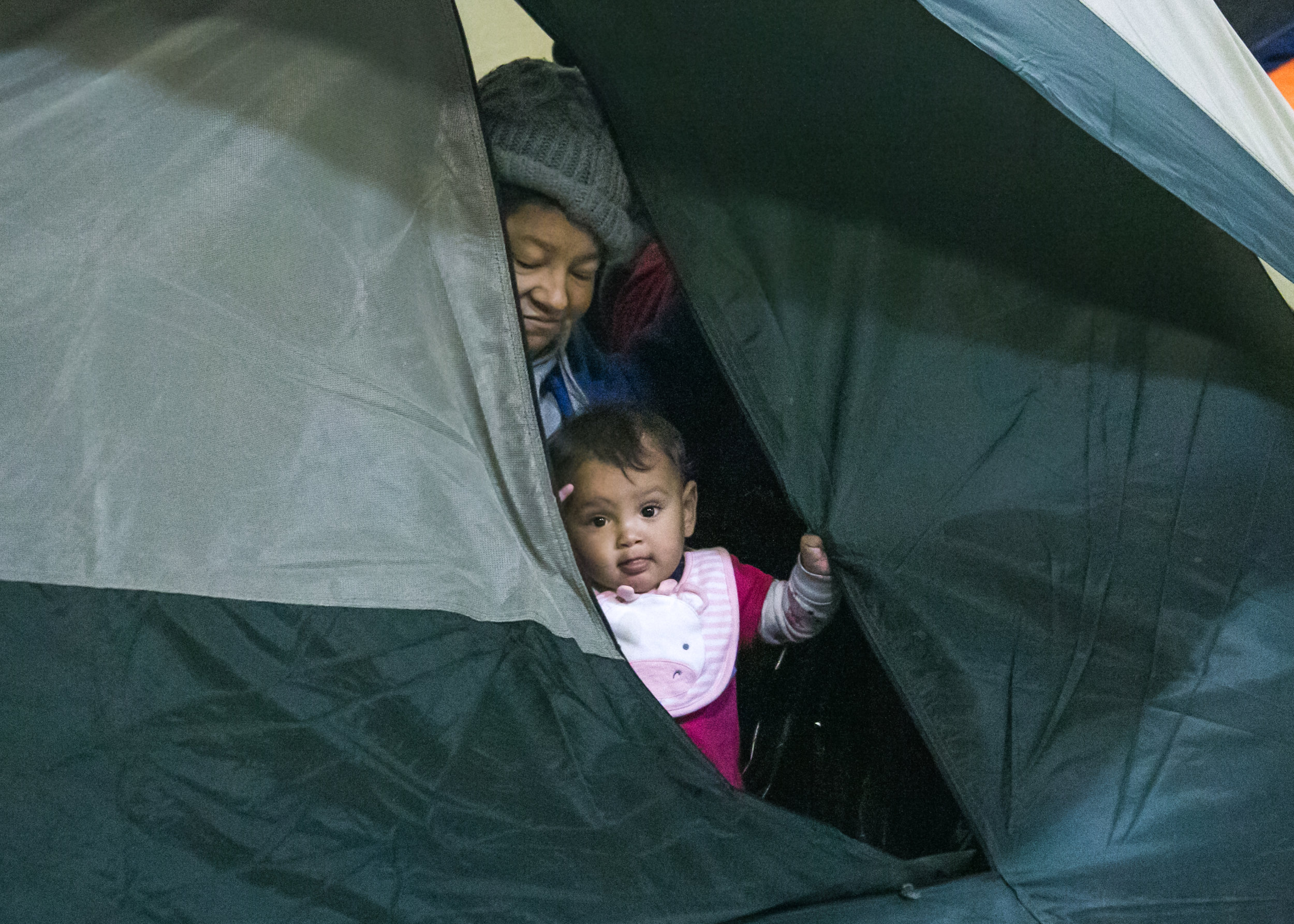  A child and her grandmother peer out of their tent to watch children playing outside. The Barretal camp now houses between 1,500 and 2,000 migrants - with 30-40 leaving and coming each day. 