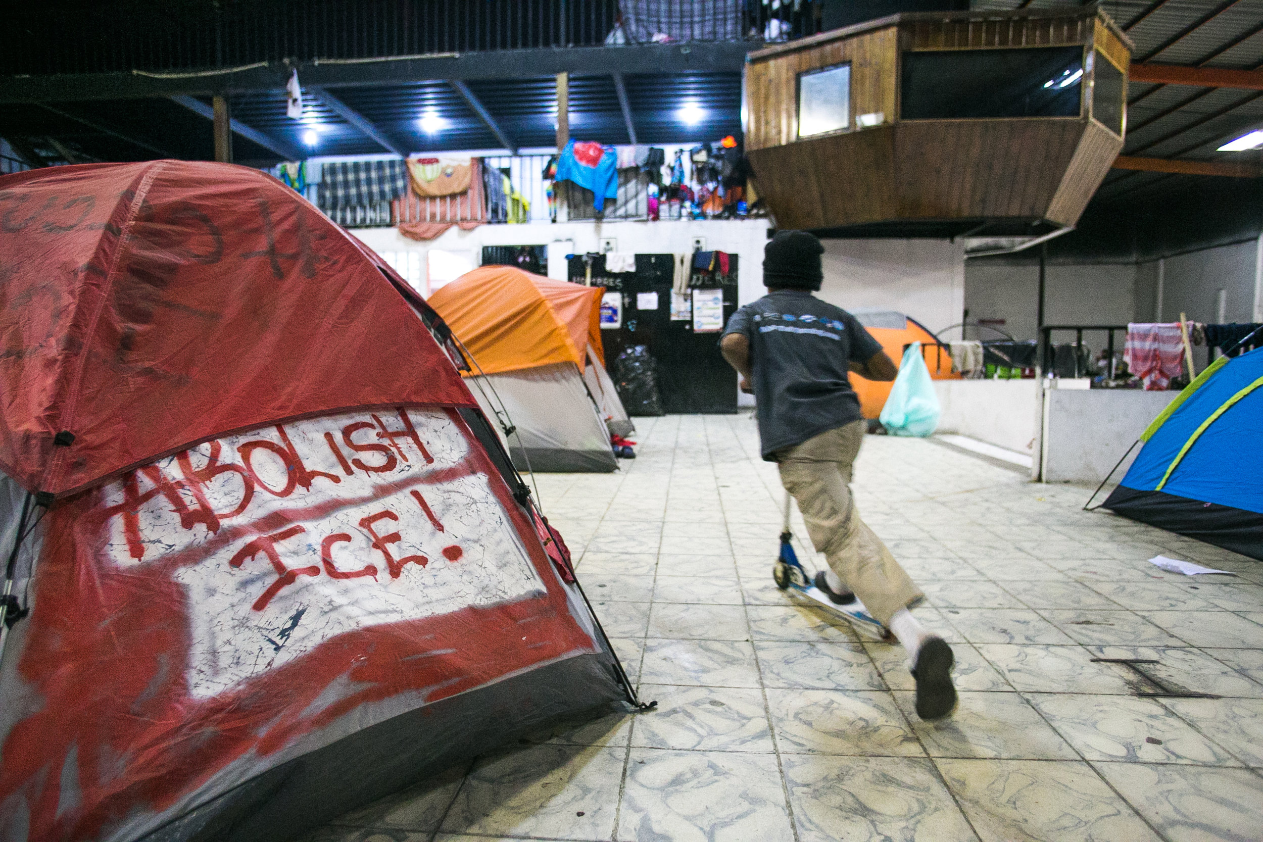  A boy scooters by a tent spray painted with the text “Abolish ICE” in the Barretal migrant camp located 15 miles outside Tijuana, Mexico. This section of the camp houses woman, children, and elderly. Many of the families have been waiting for their 