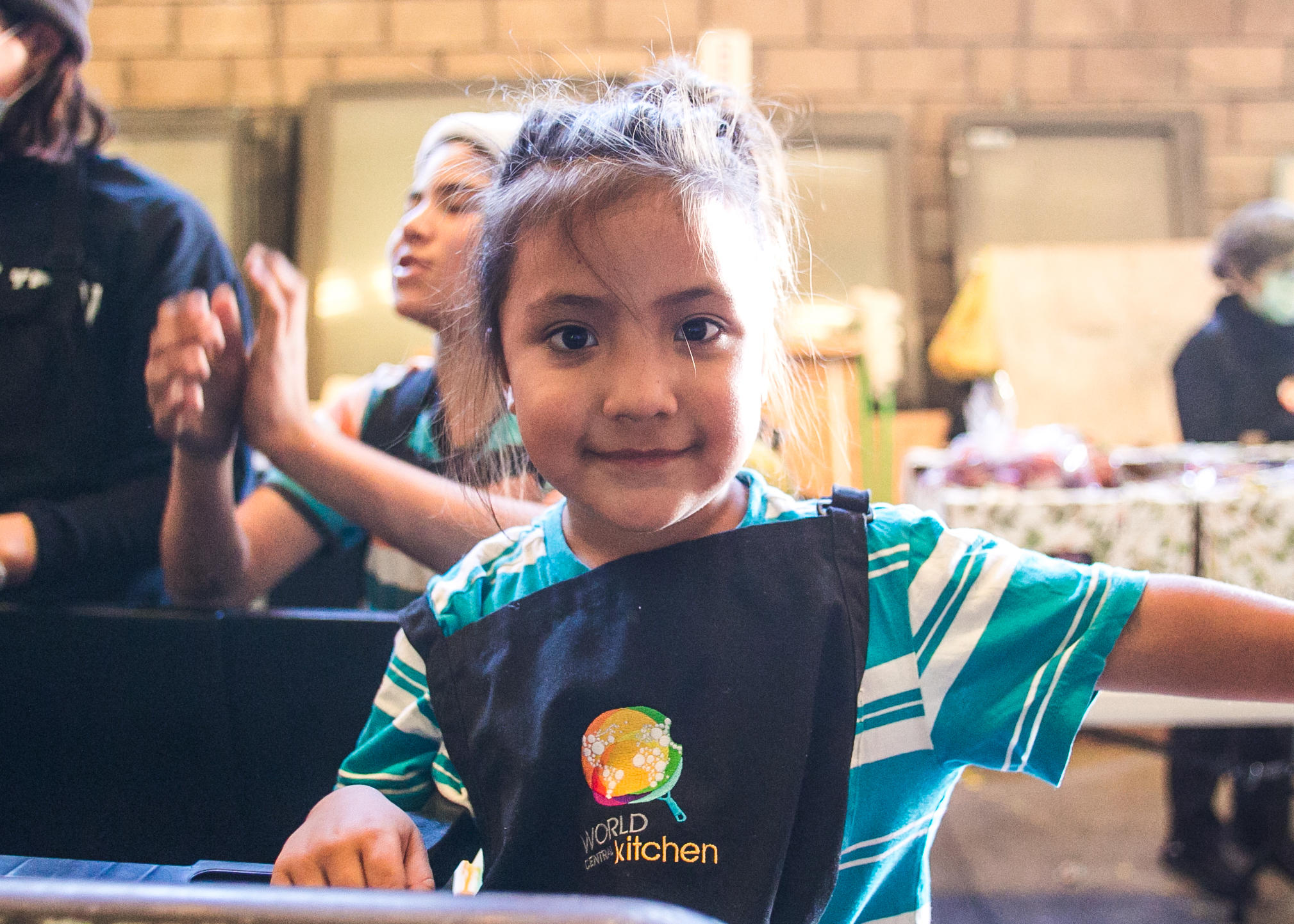  A volunteer and occupant of the El Chinchetta  facility helps serve lunch to over 1,500 refugees. Each day, 5-6 children from the camp would assist World Central Kitchen with serving lunch. The goal of the program surrounds creating a sustainable re