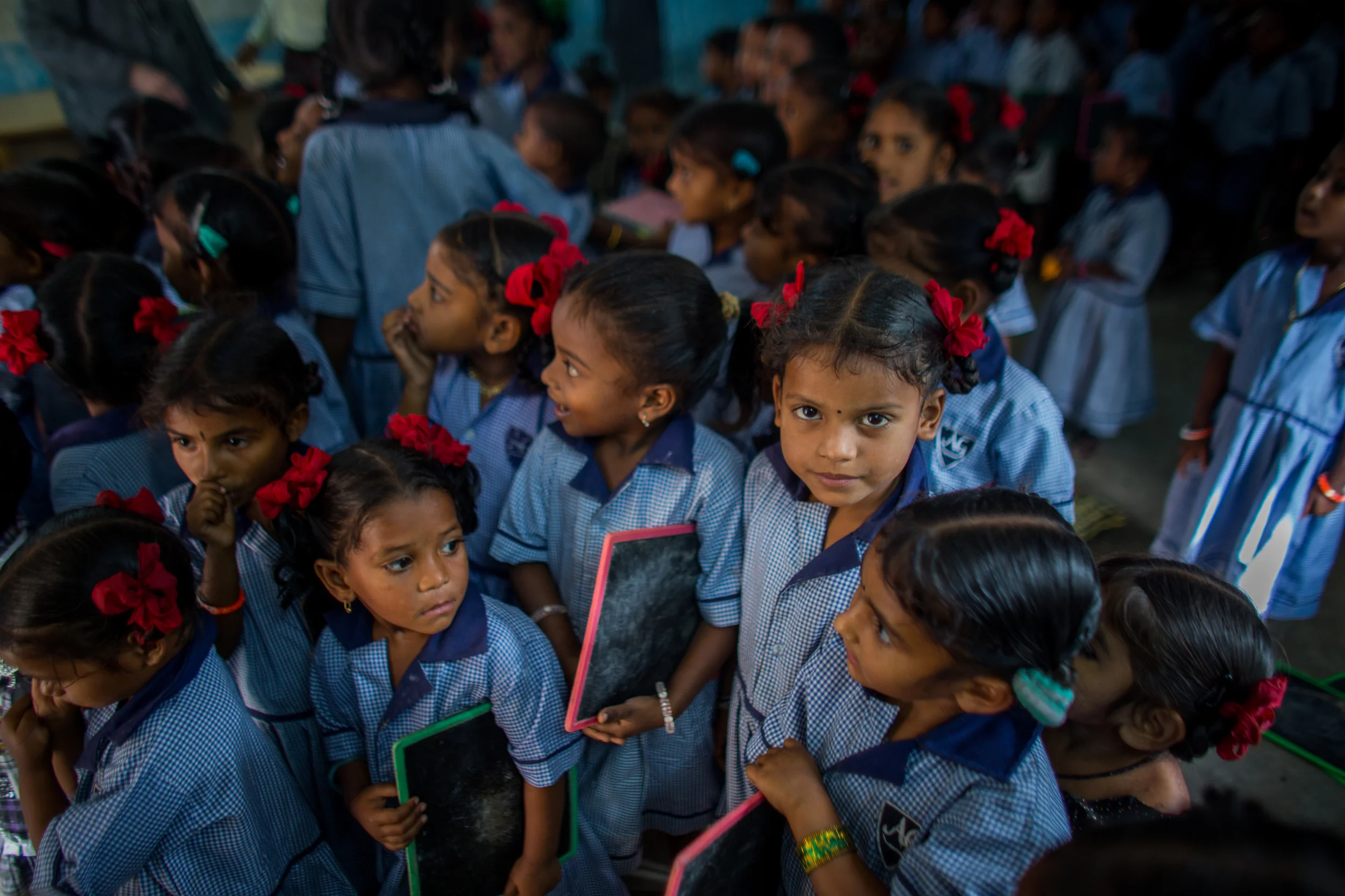 30 children gather in front of a Mercy School outfitted with colorful rugs, posters, a chalkboard, books, and school supplies.