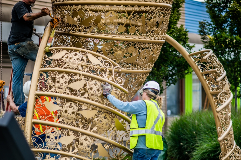 “Allure” is fabricated from ornamental iron and sheet metal laser cut with integrated motifs including many designed by South Park community members, symbolic of the rich history and cultural diversity of the area. The open iron filigree is covered with a brilliant metallic gold glaze. In this photo, Diane leads install crew on the siting of the artwork.