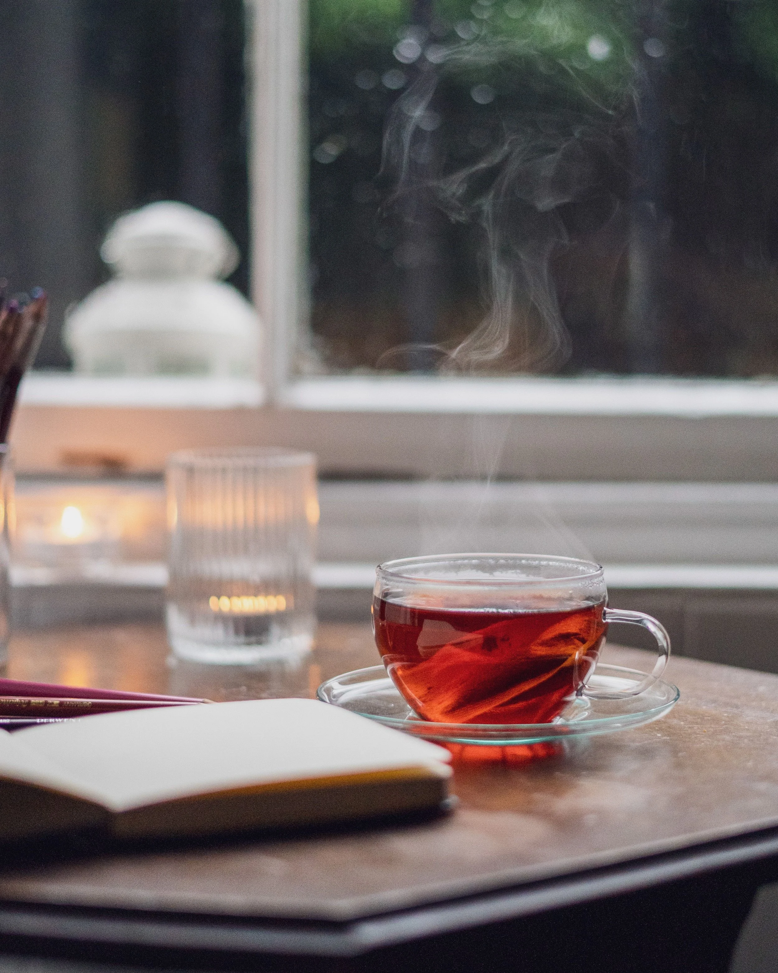 a steaming cup of tea and an open journal by a window