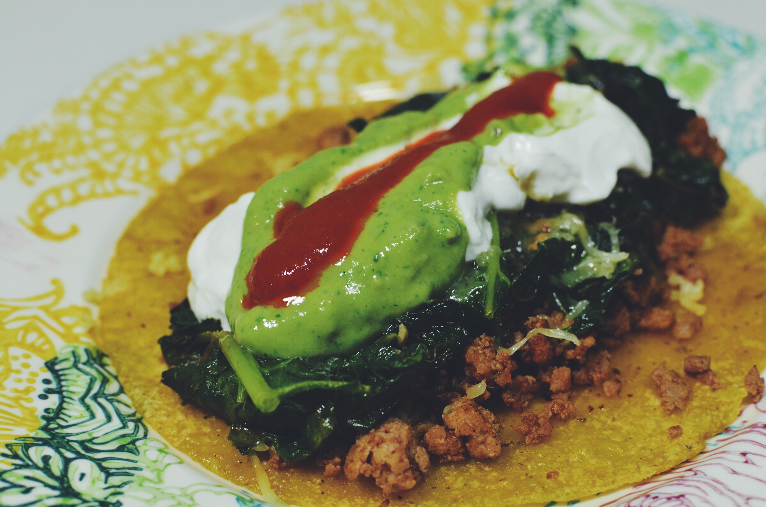 A sprouted corn tortilla topped with ground turkey, sautéed kale, grassfed cheese, greek yogurt, avocado dressing and a squeeze of Sriracha sauce.