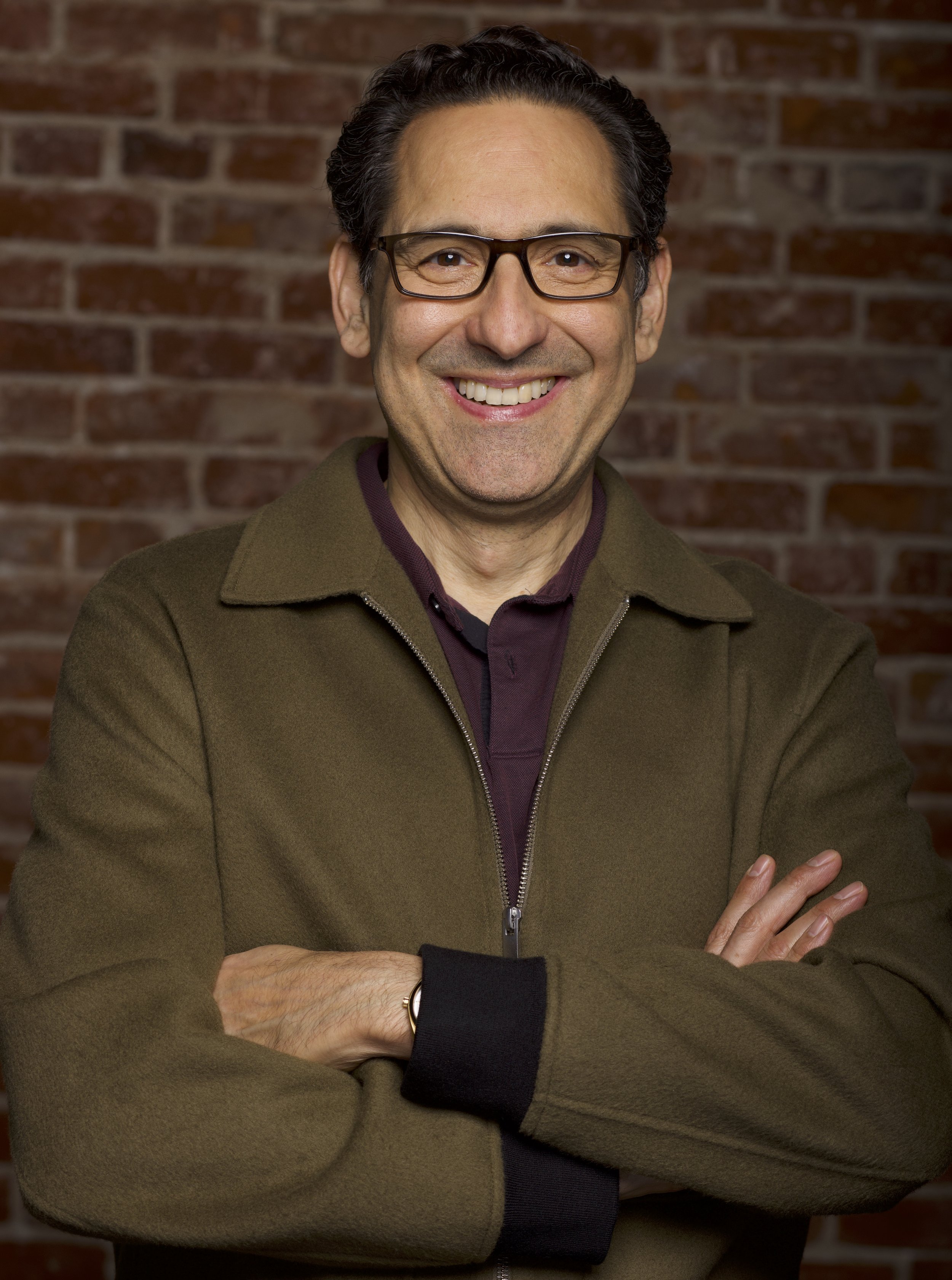Man smiling against green background, wearing a patterned blue shirt.