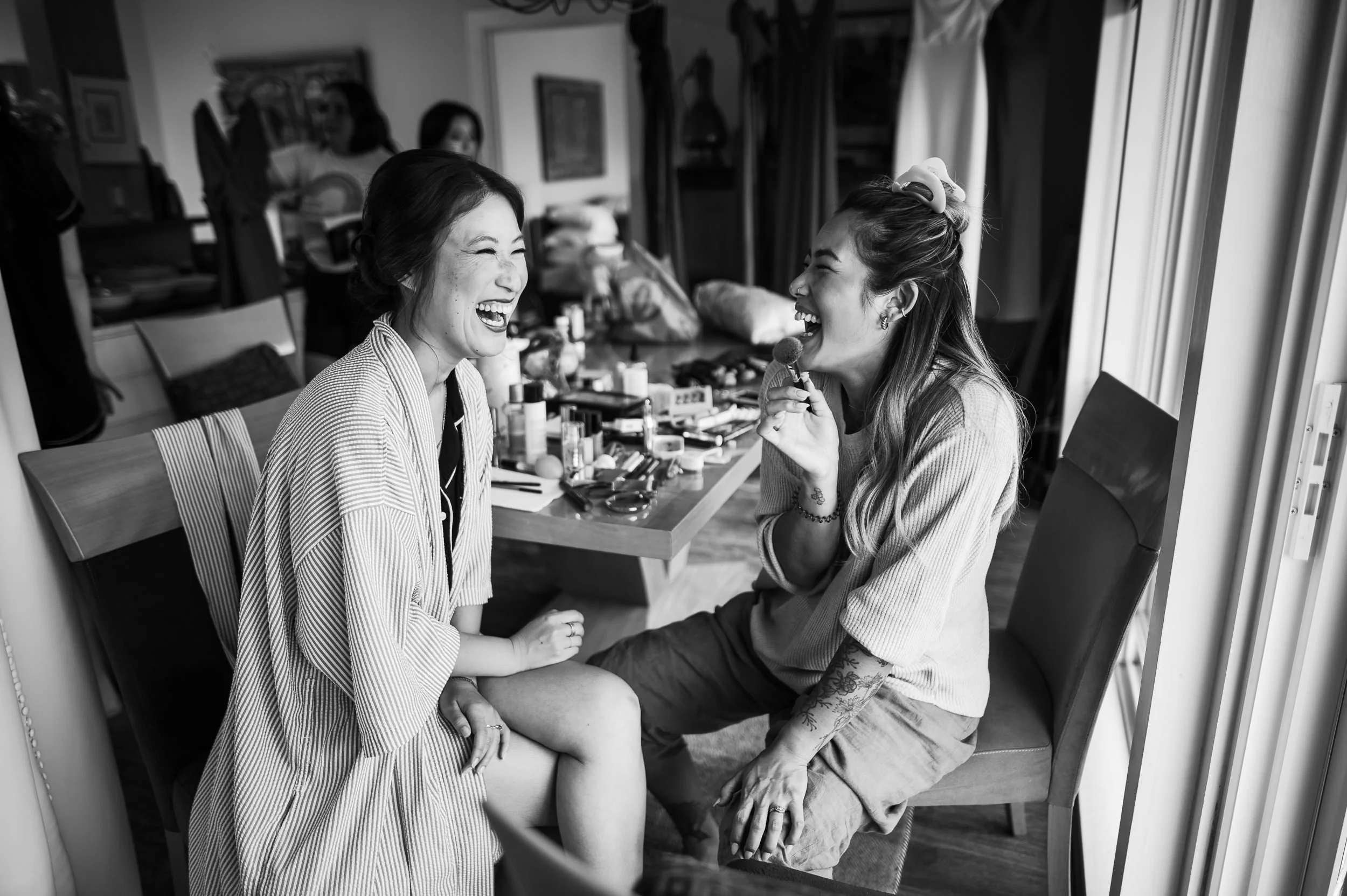 Bride and her bridesmaid sharing a laugh as they get ready for a wedding
