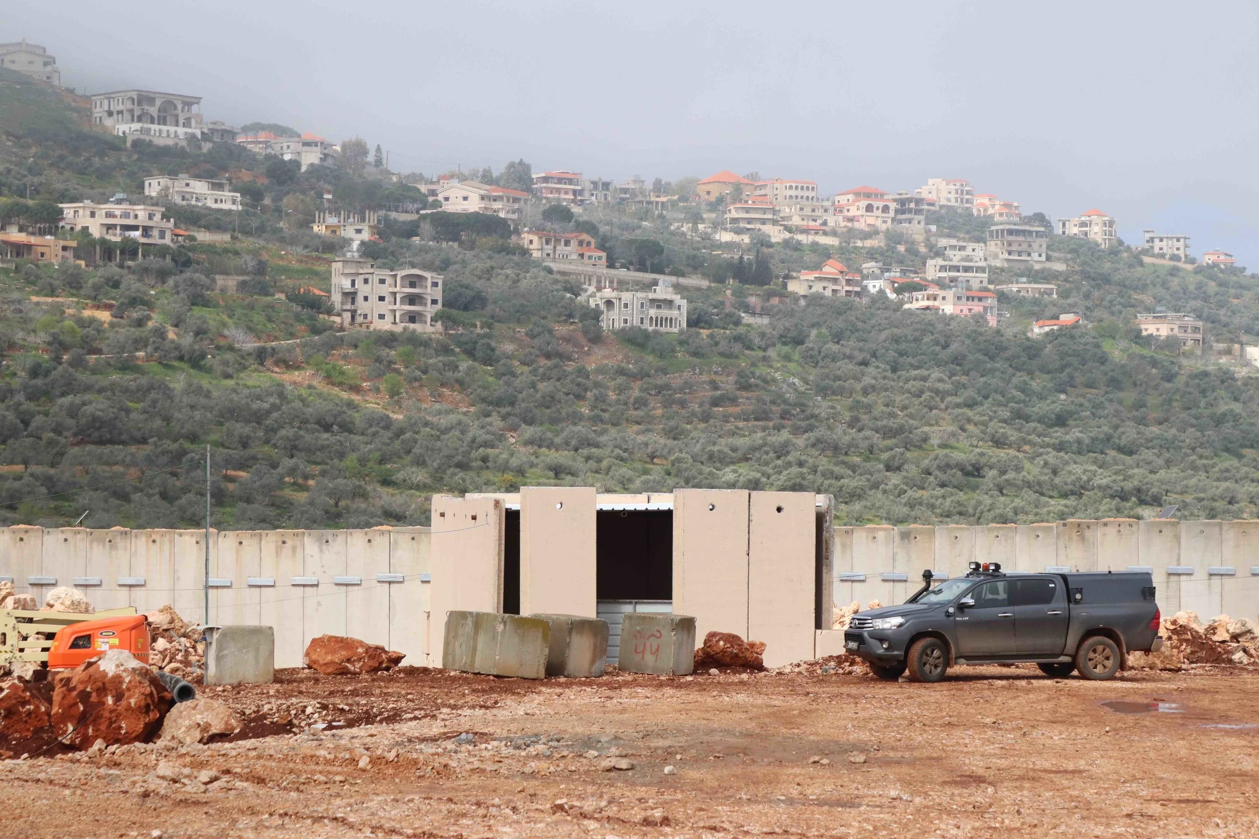 View over border wall from Metula to Lebanon. Israeli crews work to fill a tunnel.