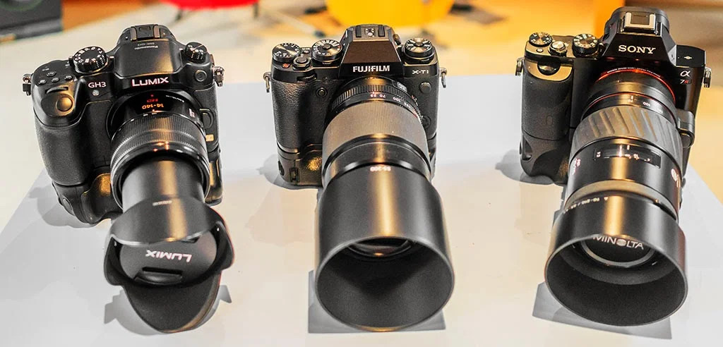 Fuji X-T1, Panasonic GH3, Sony A7r with battery grips and zoom lenses.