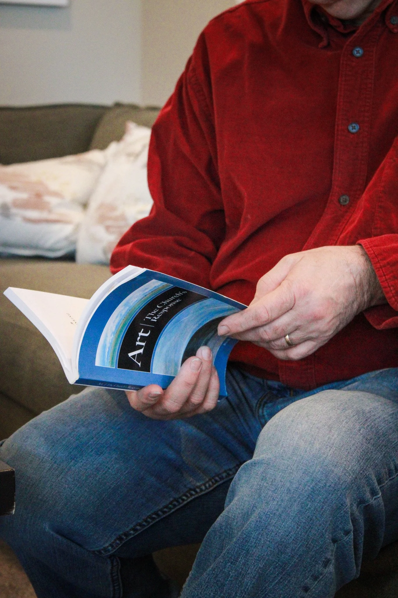 Person wearing a red shirt, sitting on a couch and reading a book titled "Art: The Churkar Response."