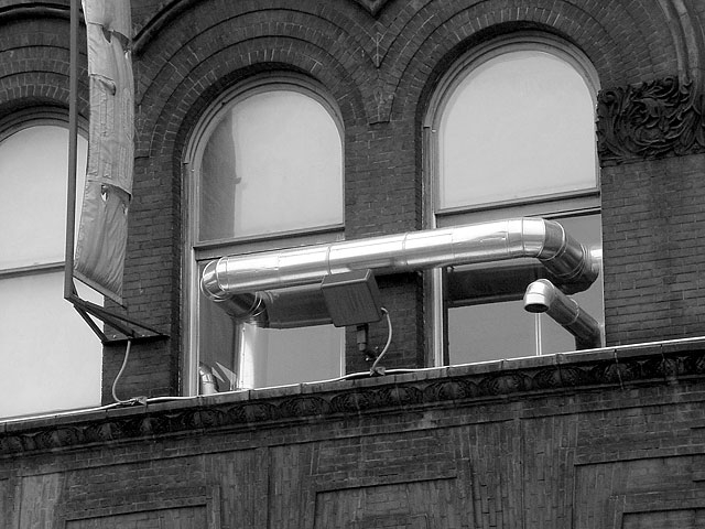 In order to lower the temperature of the Special Projects room to which it is confined, Climate Control , an apparatus consisting of ductwork and fans, incorporates the existing radiator system on the interior of the building with the cold winter temperature outside. The resulting maze of ductwork features a central absurd element: the continuous duct which travels outside the windows and then directly back in, visible from the street. An internal humidifier feeds off moisture in the air and maintains a relative humidity of 20%, in keeping with the standard for exhibiting artworks made from galvanized steel. While the system is adjustable and can maintain a stabilized environment for the display of even delicate works on paper, there is no space to exhibit other art: Climate Control completely engulfs the room. The result is an absurd machine built to maintain itself.