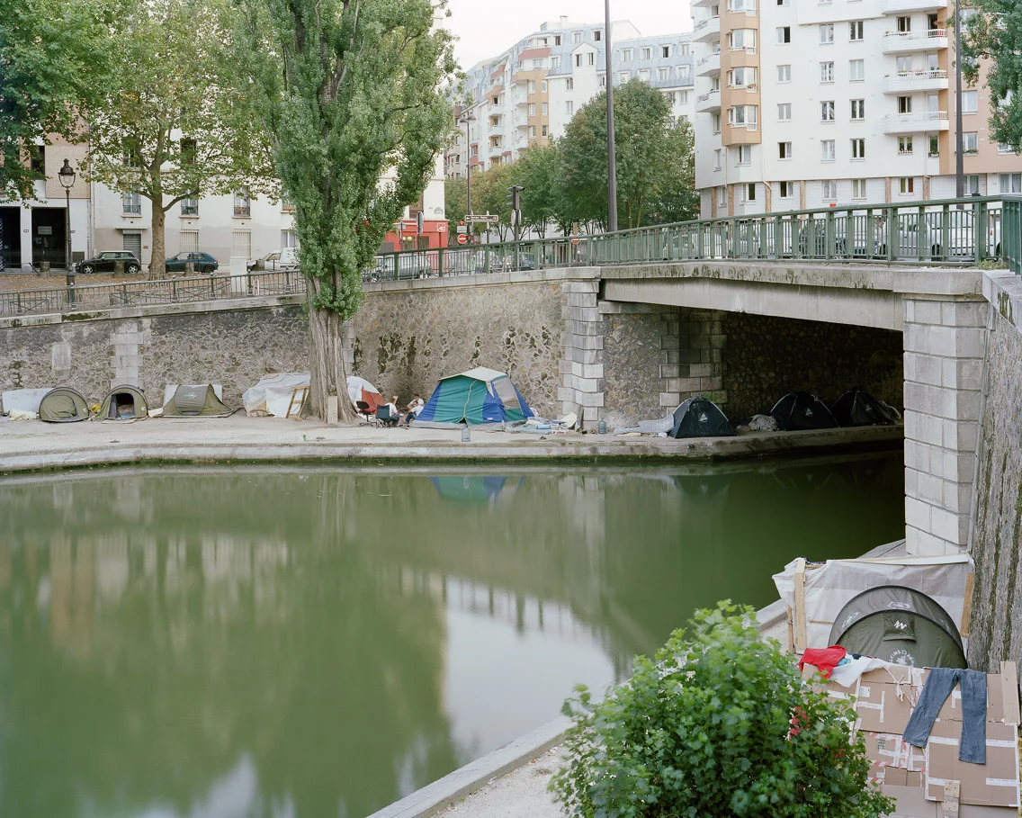 Squatters #1 – Canal St. Martin, 10ème Arrondissement, Paris, 2006. 40"x50" l'habitat marginalisé artist's statement “L'enfants de Don Quixote” is the group of homeless protesters who recently set up a tent squat along the banks of the Canal St. Martin. They chose this bourgeois neighbourhood precisely because the presence of their squat would be so confrontational there. As their cause gained momentum, they were joined by many university students and others in solidarity – hundreds of people living in tents during the (unusually mild) Parisian winter to demonstrate the deplorable situation of the homeless in Paris. Their highly visible protest was also highly successful, as just after Christmas 2006 the French National Assembly passed a law enshrining the right to housing beside that of healthcare and education. 