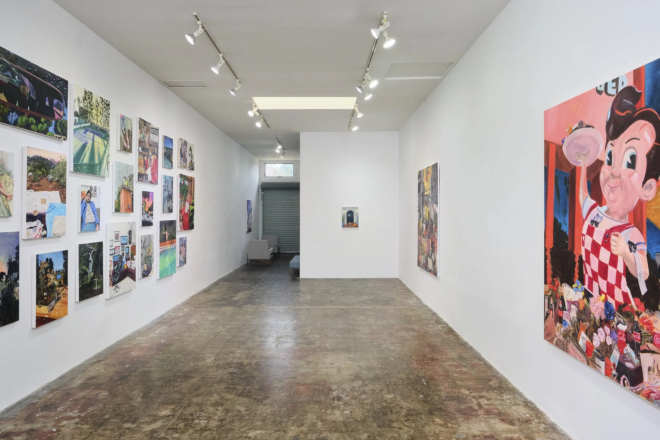 An art gallery with white walls displaying colorful paintings, track lighting on the ceiling, and a wooden floor.