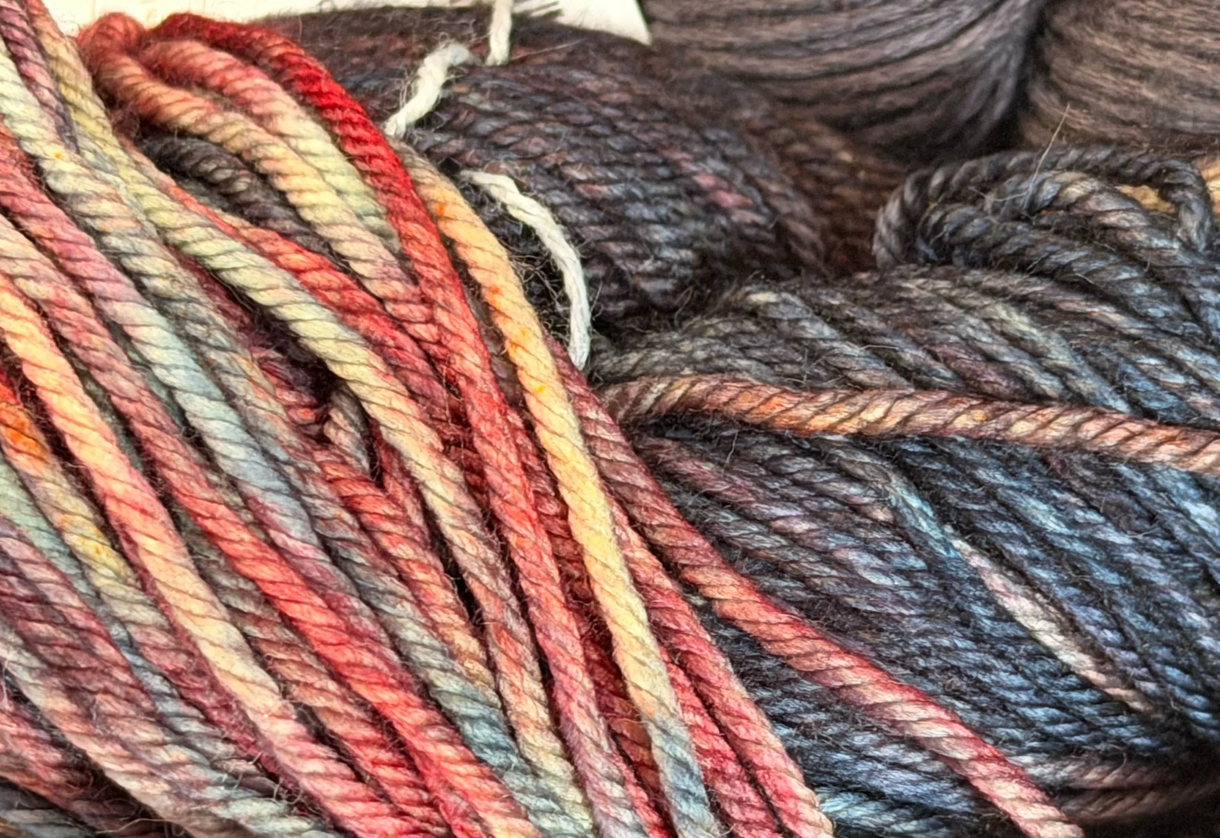 Close up of hand dyed yarn featuring bright reds and orange tones with purple and nearly black tones.