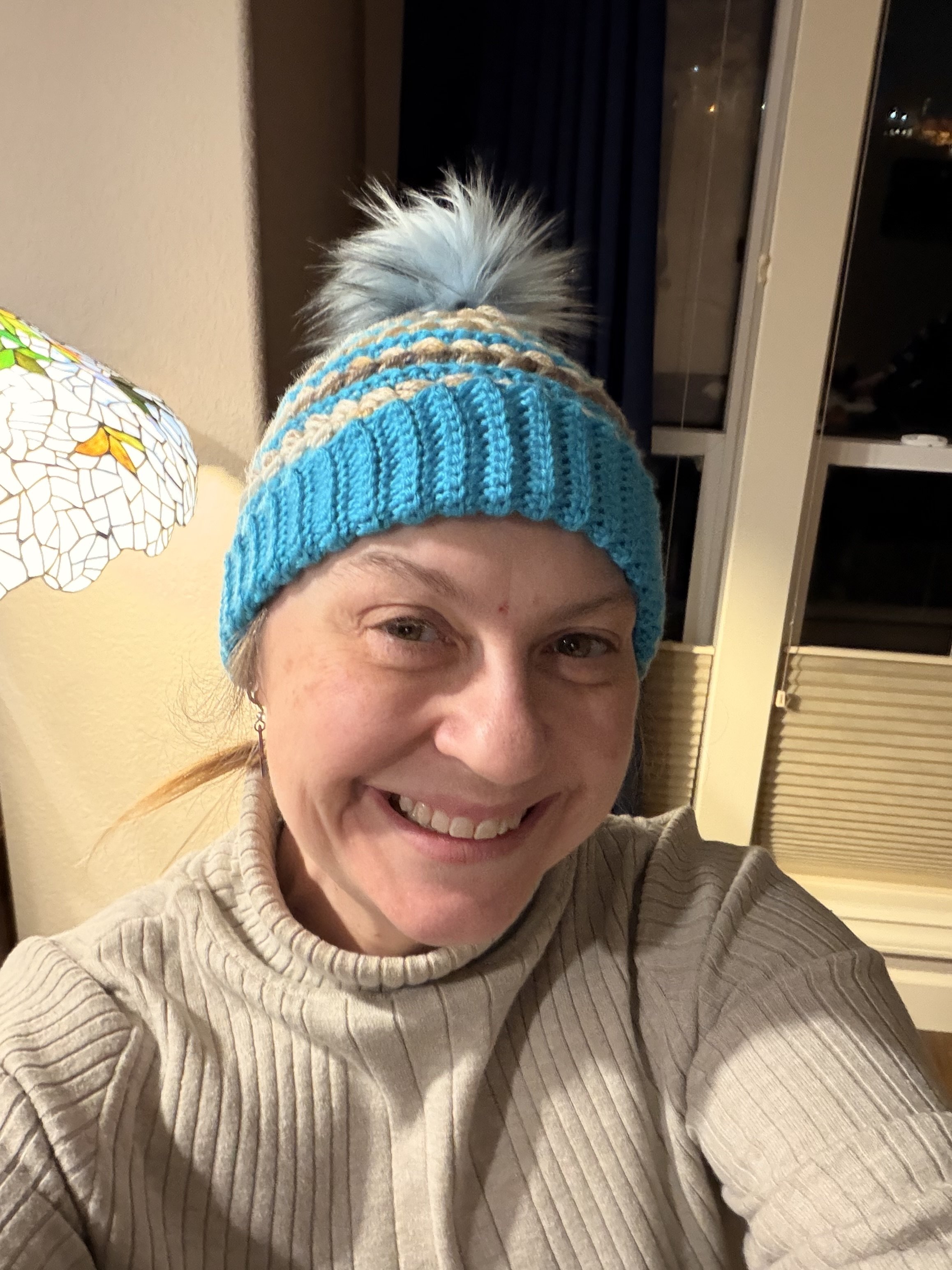 Julie wearing a blue and tan striped crochet hat with a fuzzy ball at the point.