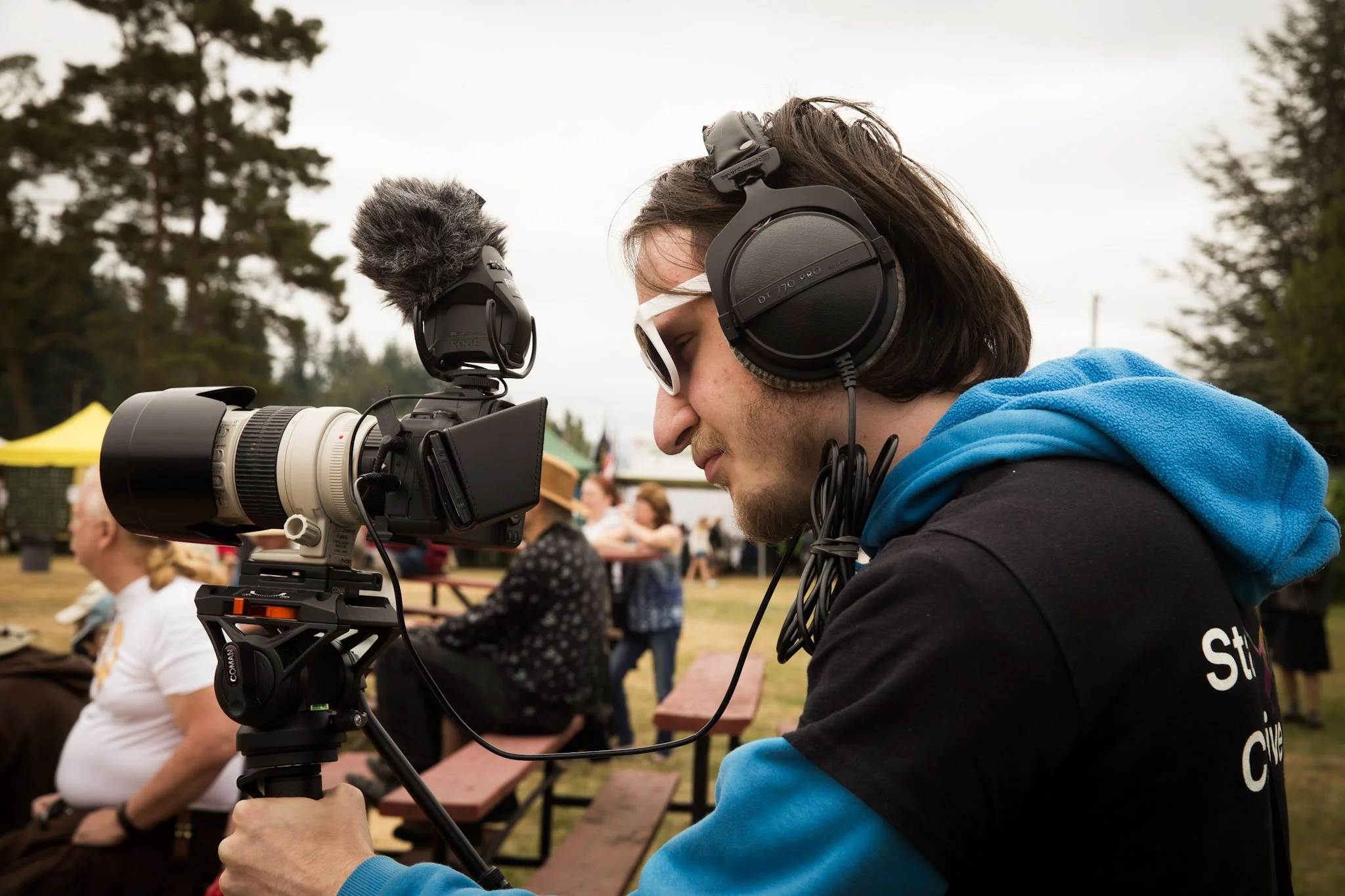A crew member recording a video at a festival using a monopod supported camera and headphones.