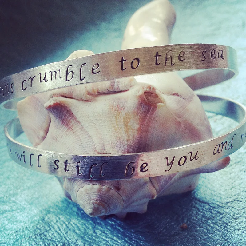 Set of two hand stamped sterling silver bangles with song lyrics.