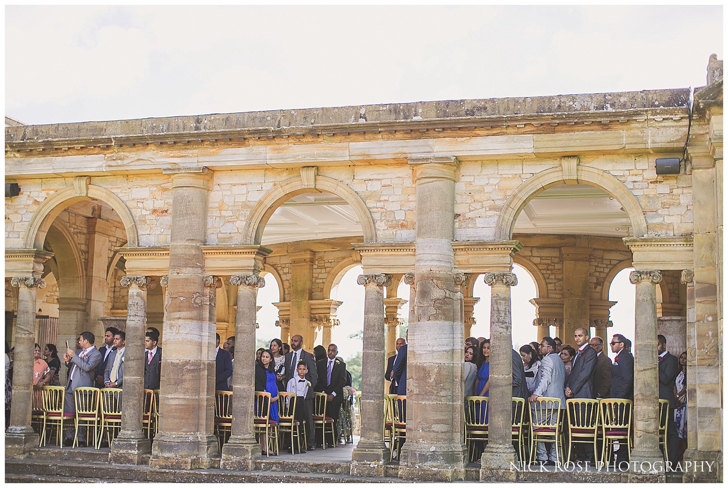  Guests watching bride walk up the red carpet in the Hever Castle Italian gardens in Kent 