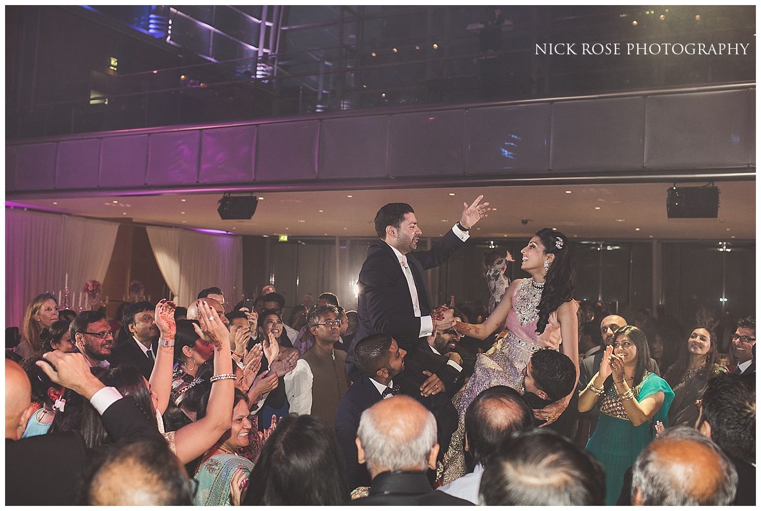  Bride and groom raised onto guests shoulders during an Indian wedding reception in East Wintergarden Canary Wharf London 